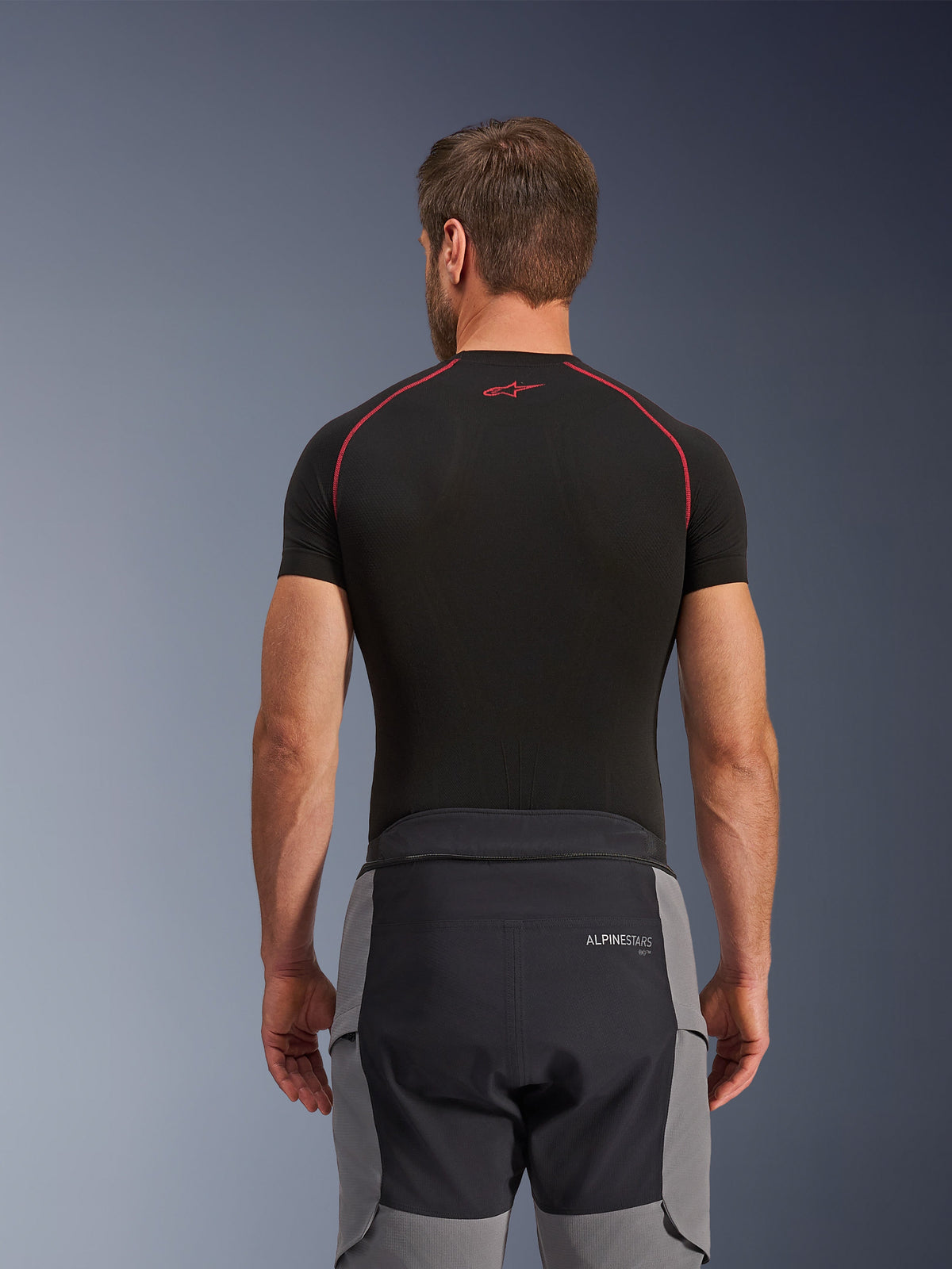 Alpinestars Andes Pro Drystar® XF Pants, pantaloni da moto adventure, grigio scuro e nero, vista posteriore che mostra la struttura della vita e i pannelli laterali grigi, indossati con un base layer nero con cuciture rosse, abbigliamento tecnico da touring per ogni condizione meteorologica.