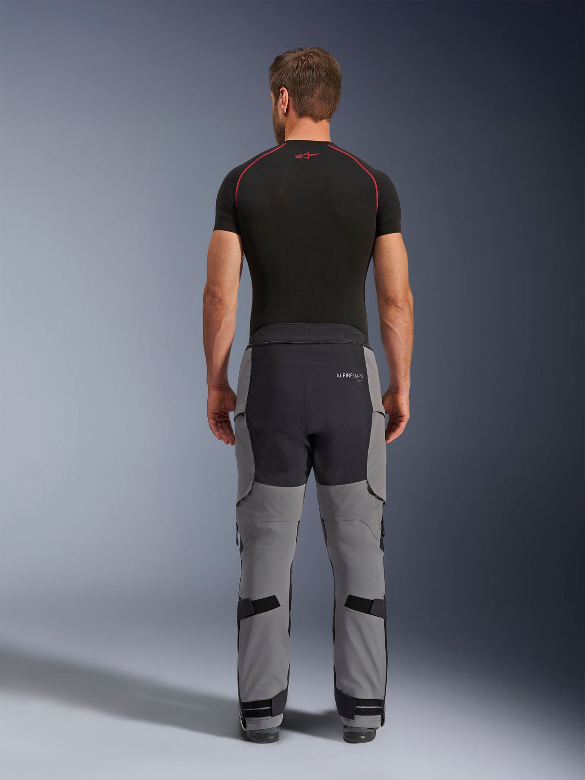 Pantaloni Alpinestars Andes Pro Drystar® XF, pantaloni da moto adventure, grigio scuro e nero, vista posteriore con costruzione a pannelli grigi e neri, indossati con un base layer nero, dotati di seduta rinforzata e cinghie di regolazione sui polpacci per il touring.