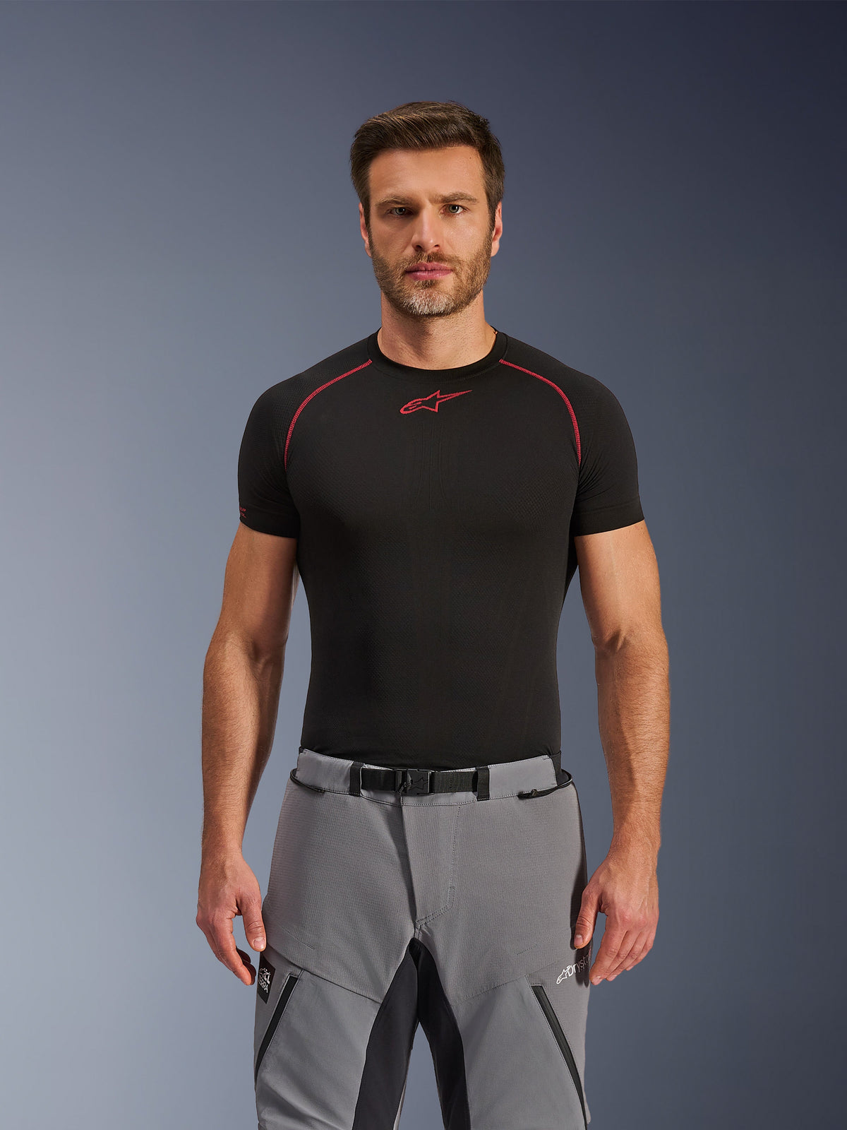Pantaloni Alpinestars Andes Pro Drystar® XF, pantaloni da moto adventure, grigio scuro e nero, indossati da un modello con base layer tecnico nero, chiusura in vita con fibbia magnetica, costruzione in tessuto resistente e marchio Drystar® XF per il turismo in ogni condizione atmosferica.