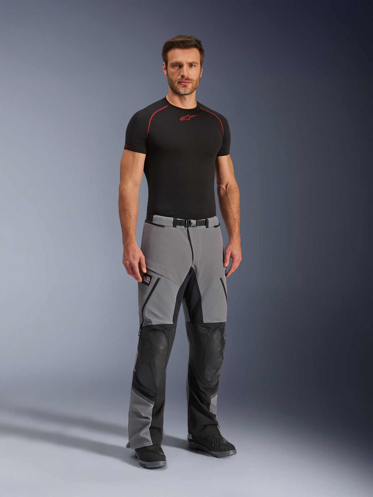 Alpinestars Andes Pro Drystar® XF Pants, pantaloni da moto adventure, grigio scuro e nero, indossati da un modello con un base layer tecnico nero, caratterizzati da una costruzione multi-pannello con cerniere impermeabili e zone rinforzate per il motociclismo d'avventura.