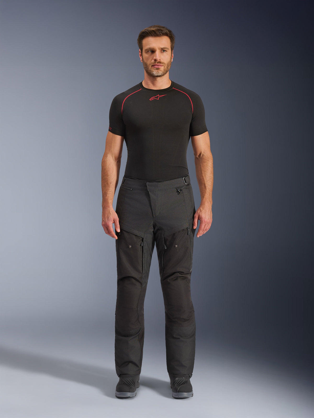 Pantaloni Alpinestars Cusco Drystar®, pantaloni da moto in tessuto, nero, indossati da un modello con base layer e stivali neri, design adventure touring con pannelli di ventilazione con zip sulle cosce e costruzione multi-pannello resistente