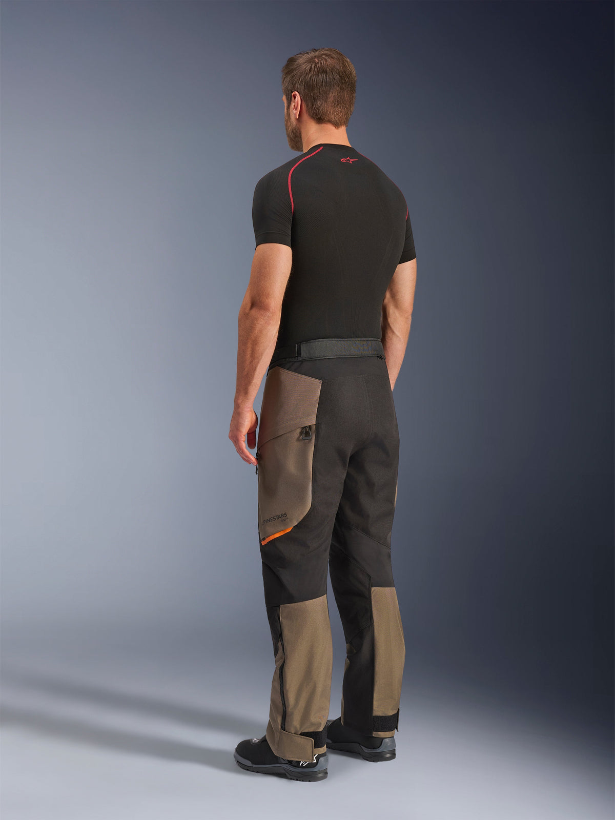 Pantaloni Alpinestars Cusco Drystar®, pantaloni da moto adventure, Walnut Black, vista posteriore a tre quarti indossati con base layer nero e stivali, con pannelli in tessuto rinforzato, tasche cargo con zip sulle cosce e vestibilità touring ergonomica.