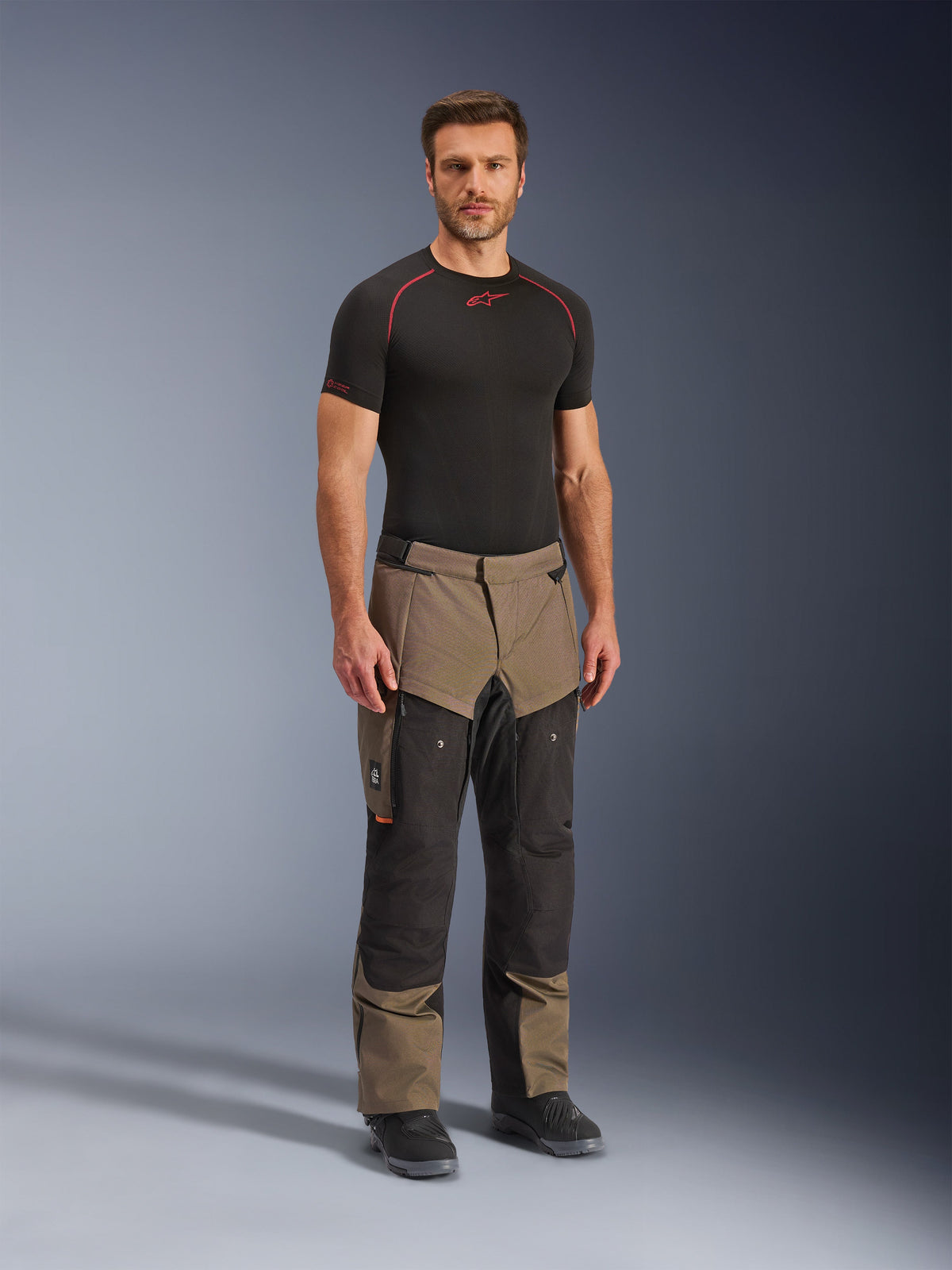 Pantaloni Alpinestars Cusco Drystar®, pantaloni da moto adventure, colore noce e nero, indossati da un modello con base layer nero e stivali, con ampie tasche cargo sulle cosce, zip di ventilazione e design bicolore robusto.