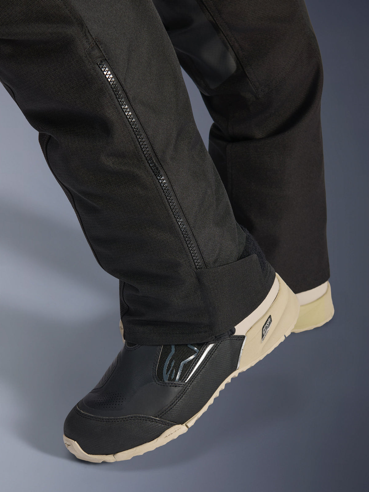 Alpinestars Stella Andes V4 Drystar® Pants, neri, primo piano della parte inferiore della gamba con cerniera laterale per la regolazione dello stivale, materiale tessile resistente, indossati con stivali da moto neri e sabbia, design funzionale per l'avventura