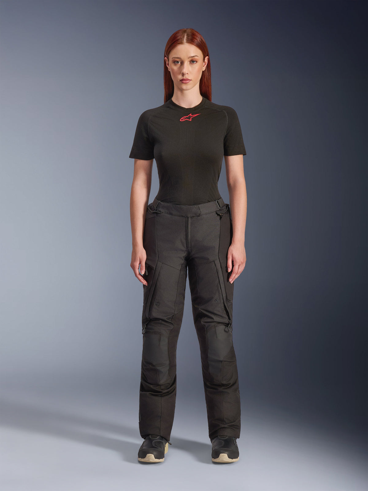 Pantaloni Alpinestars Stella Andes V4 Drystar®, pantaloni da moto adventure touring da donna neri, mostrati su una modella con t-shirt Alpinestars nera, design in tessuto tecnico con tasche cargo e pannelli rinforzati sulle ginocchia.