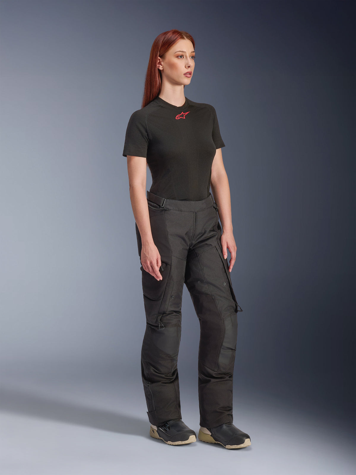 Pantaloni Alpinestars Stella Andes V4 Drystar®, pantaloni da moto da donna, neri, indossati con una t-shirt nera a maniche corte con logo rosso e scarpe tecniche, design adventure touring con pannelli rinforzati e zip di ventilazione, vista a tre quarti a figura intera