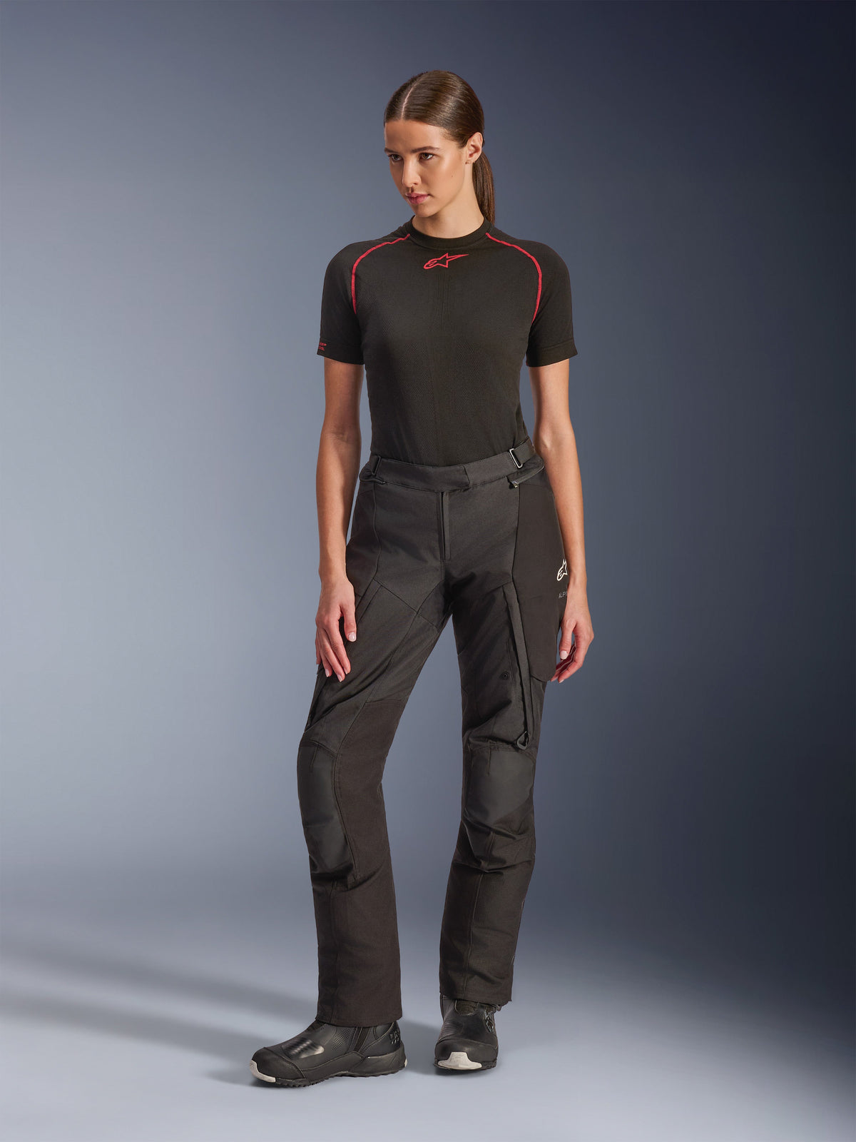 Alpinestars Stella Andes V4 Drystar® Pants, pantaloni da moto adventure da donna, neri, indossati da una modella con base layer nero a maniche corte e stivali da moto neri, con ginocchia rinforzate e tasche cargo, design ergonomico per il touring in ogni condizione meteorologica.