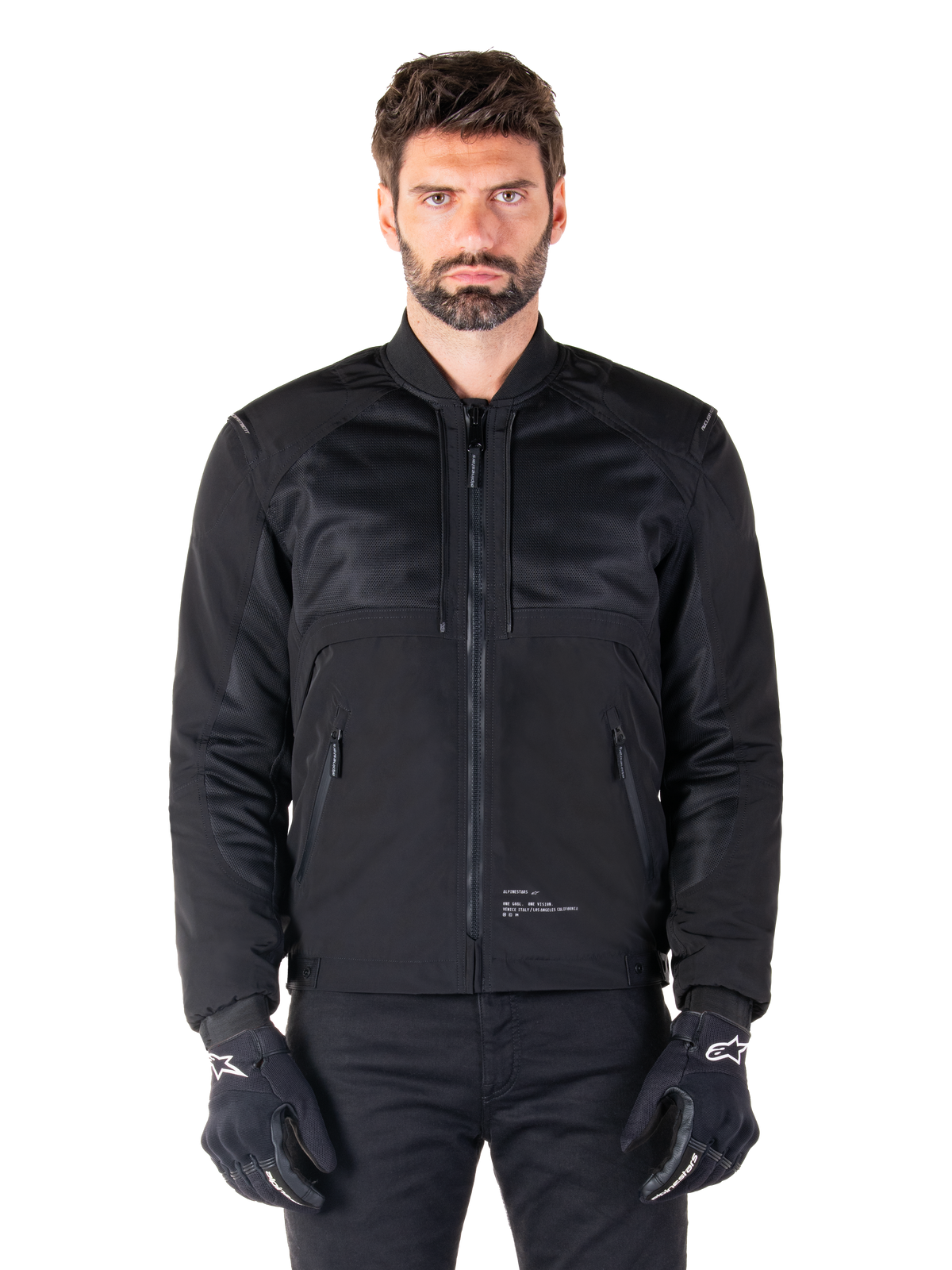 Parka impermeabile Alpinestars Mootant, giacca da moto nera, vista frontale su modello maschile, caratterizzata da una costruzione tessile modulare con pannelli in rete per la ventilazione, colletto a costine e tasche con zip, indossata con guanti neri con marchio Alpinestars bianco