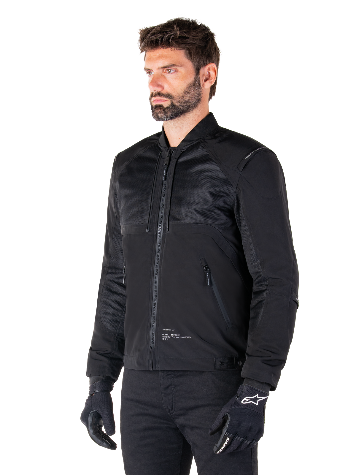 Parka Alpinestars Mootant Waterproof, giacca da moto modulare nera mostrata nella sua configurazione bomber con pannelli in rete sulla parte superiore del corpo e colletto a costine, indossata da un modello con guanti e pantaloni da guida neri, stile streetwear contemporaneo urbano.