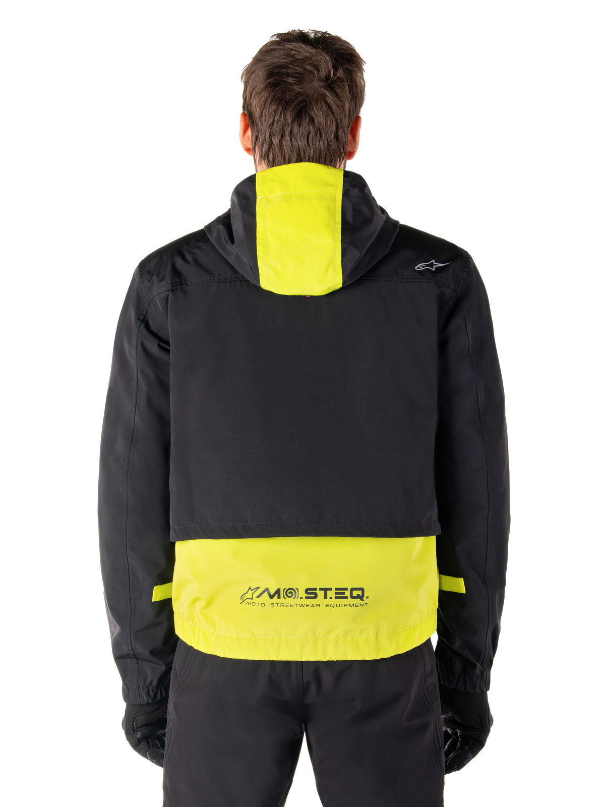 Alpinestars Mootant Waterproof Parka, giacca da moto, Lime Punch e nero, vista posteriore con design con cappuccio e marchio riflettente MO.ST.EQ. sulla parte inferiore della schiena, indossata con pantaloni da moto e guanti neri.