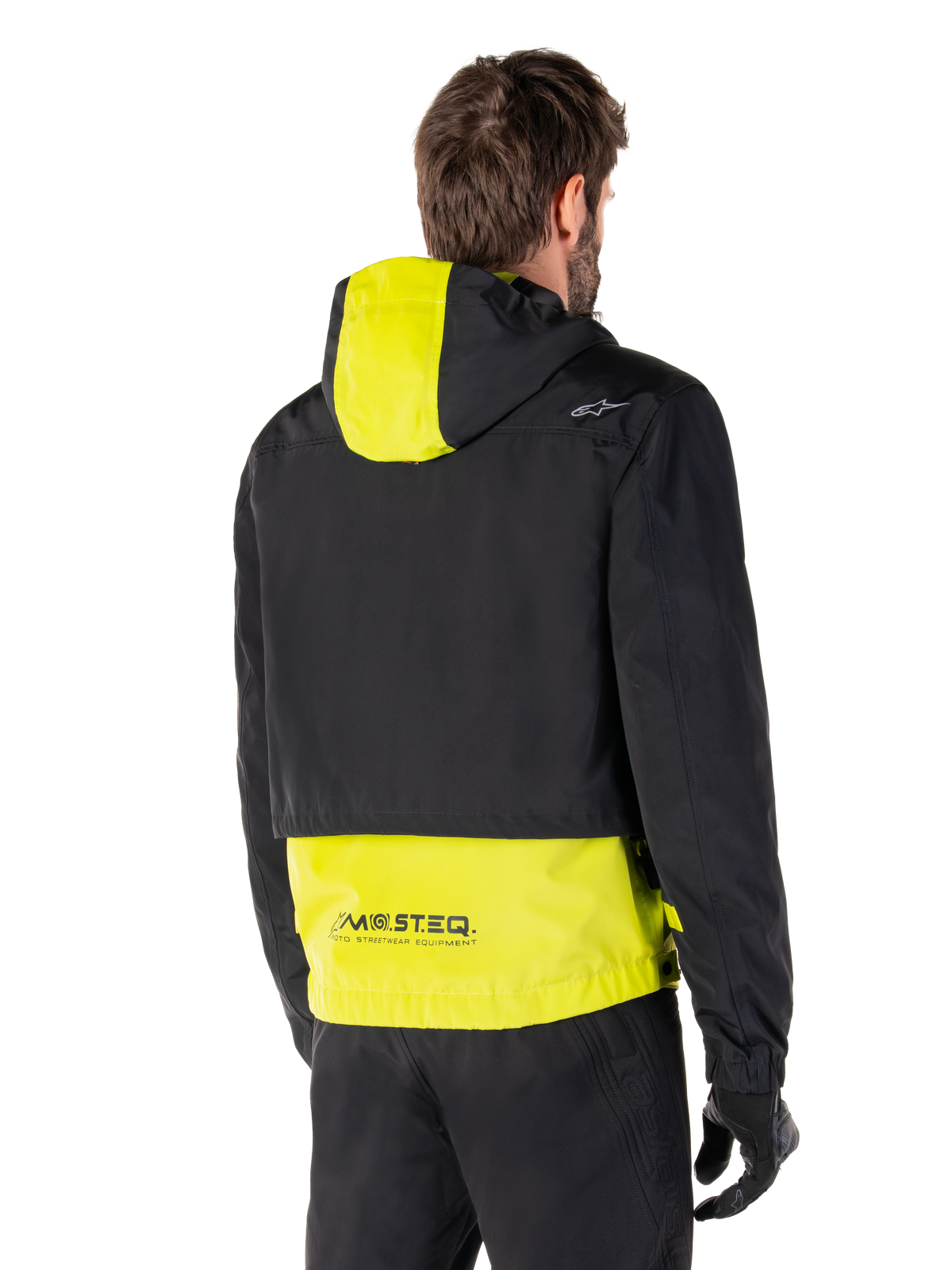 Alpinestars Mootant Waterproof Parka, vista posteriore, Lime Punch e nero, caratterizzato da una parte superiore nera con pannello del cappuccio e parte inferiore della schiena giallo lime, marchio MO.ST.EQ. sull'orlo, indossato con pantaloni da moto e guanti neri, giacca da moto urban contemporary