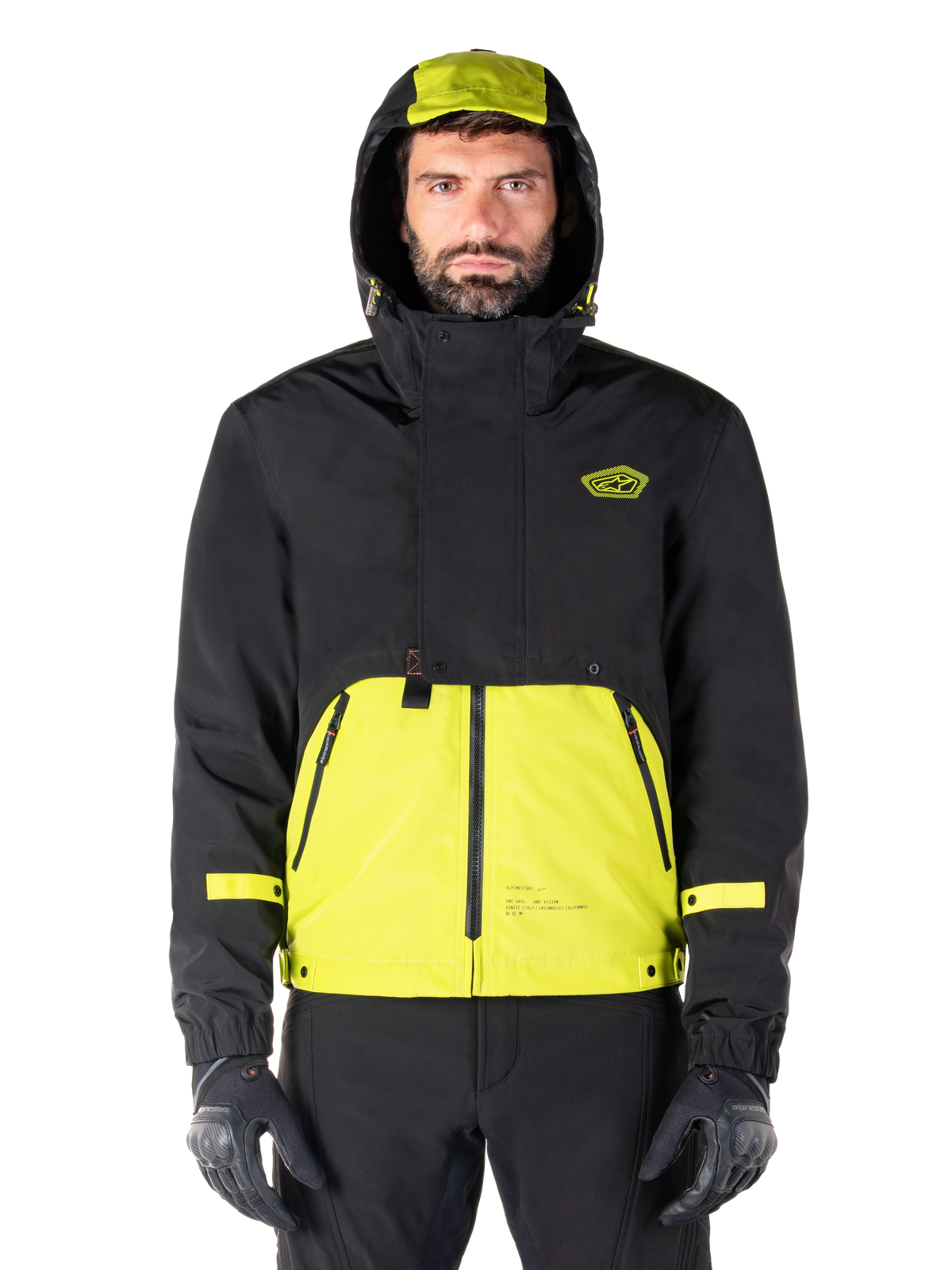 Alpinestars Mootant Waterproof Parka, giacca da moto Lime Punch Black, vista frontale, design modulare 3-in-1 con parte superiore nera e sezione inferiore verde lime brillante, dotata di cappuccio con coulisse e logo sul petto, indossata con pantaloni neri e guanti da moto