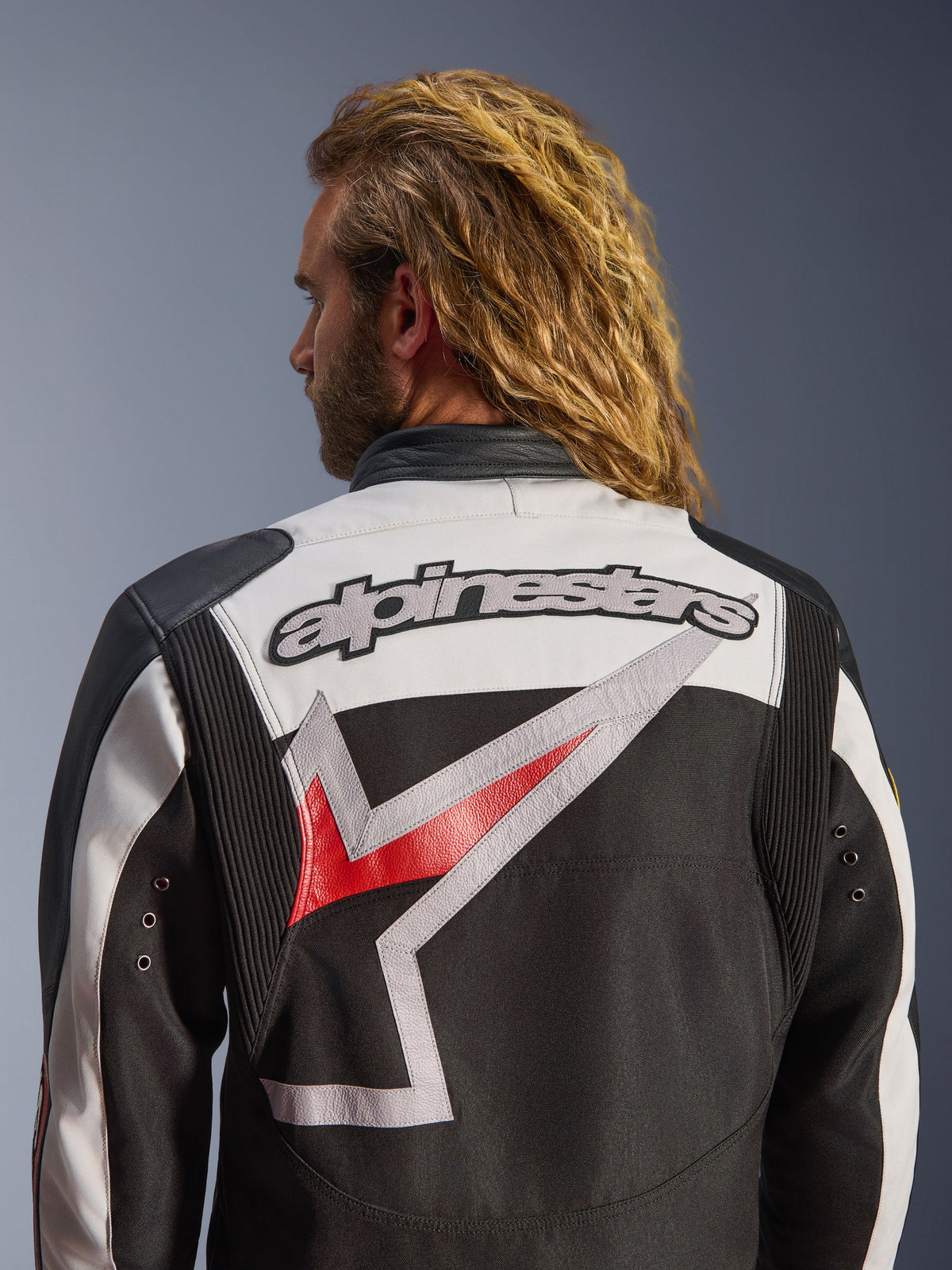 Giacca Alpinestars Axton, giacca da moto, nero, bianco avorio e rosso acceso, vista posteriore con grande logo Alpinestars ricamato e grafica stilizzata, pannelli a fisarmonica sulle spalle per la mobilità, design d'ispirazione vintage con dettagli in occhielli di metallo