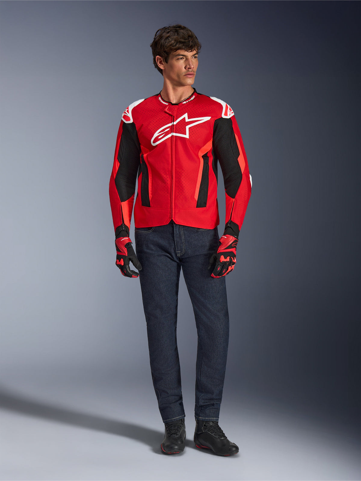 Giacca Alpinestars T-GP Air, Bright Red Red Fluo Black, modello maschile che indossa un outfit da moto completo con jeans blu scuro e guanti coordinati, giacca sportiva in tessuto con pannelli in rete traforata e logo Astars bianco, scatto in studio.