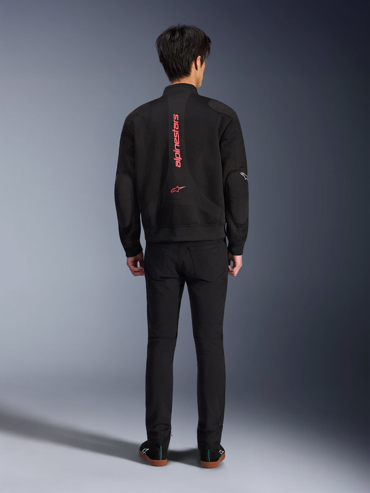 Giacca Alpinestars Flight Air in Nero Rosso Brillante, vista posteriore di giacca da moto in stile bomber urbano, con branding Alpinestars verticale rosso e logo sulla schiena, costruzione leggera in mesh 3D, indossata con pantaloni neri per un look contemporaneo.