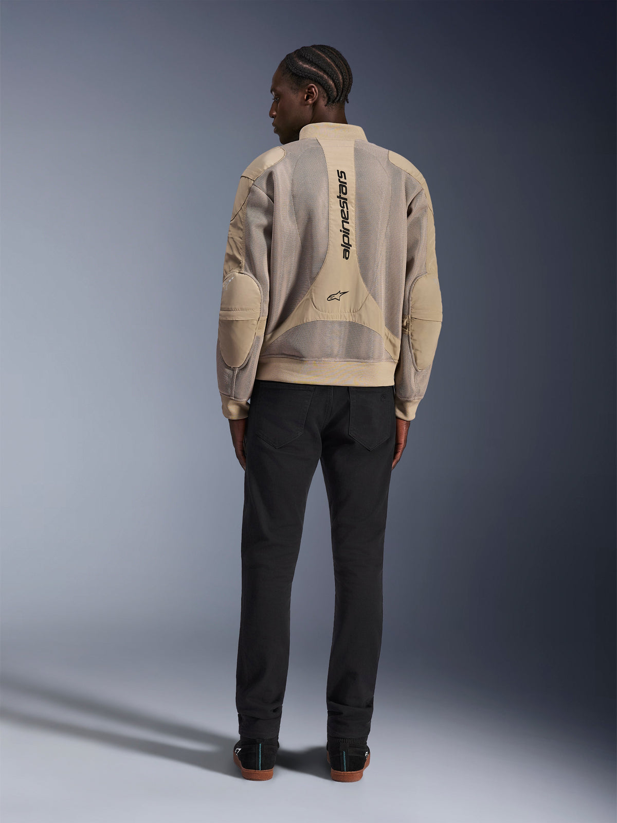 Giacca Alpinestars Flight Air, giacca da moto urbana color sabbia, vista posteriore con pannelli traspiranti in mesh 3D e logo verticale, indossata con pantaloni neri per un look moderno in stile street-style