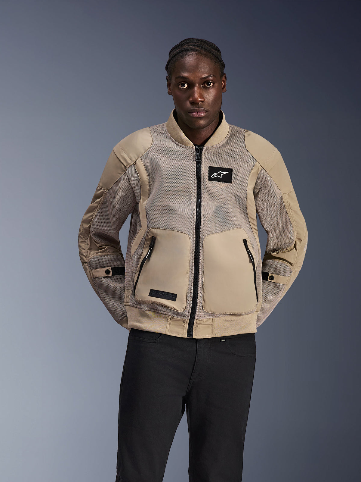 Giacca Alpinestars Flight Air, giacca da moto urbana in stile bomber, beige chiaro, con ampi pannelli in mesh 3D per la ventilazione e grandi tasche anteriori, indossata da un uomo con pantaloni neri, design moderno ispirato al motorsport per la guida in climi caldi