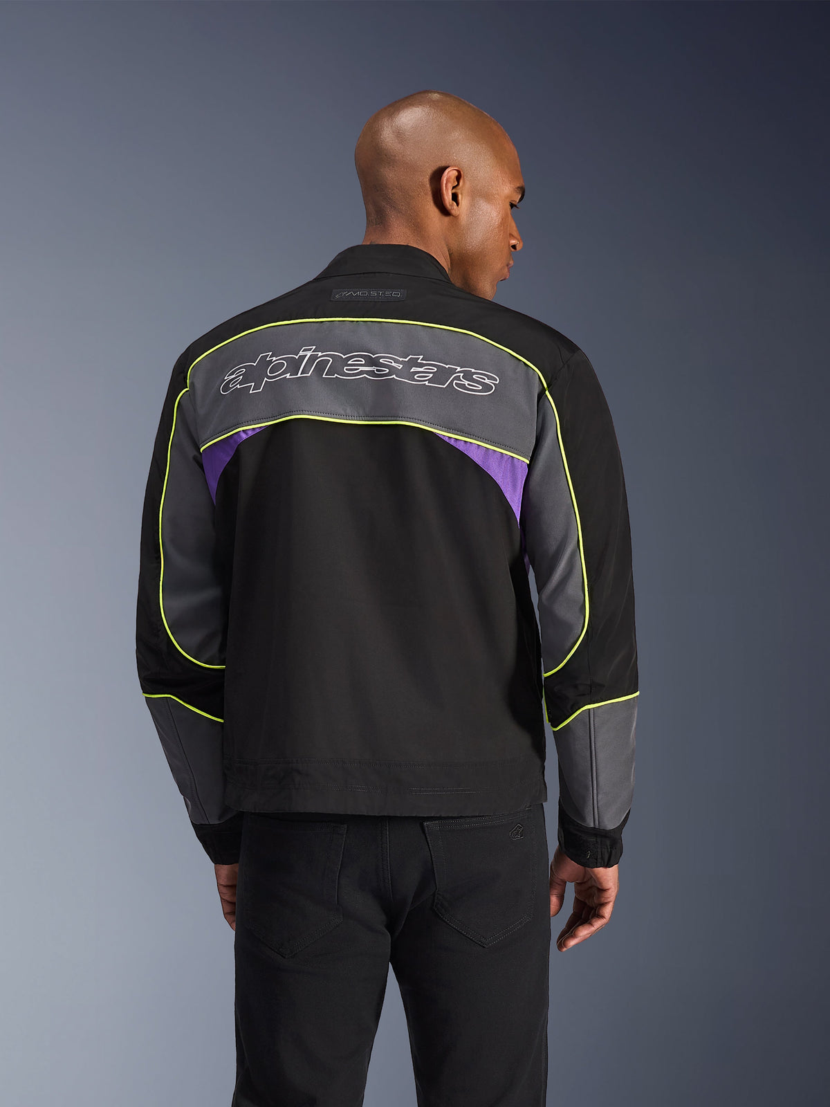 Alpinestars Giacca Unite, giacca da moto urbana, nero asphalt violet, vista posteriore con pannelli grigi e accenti viola, profili giallo lime, grande scritta Alpinestars sulla parte superiore della schiena, design streetwear minimalista