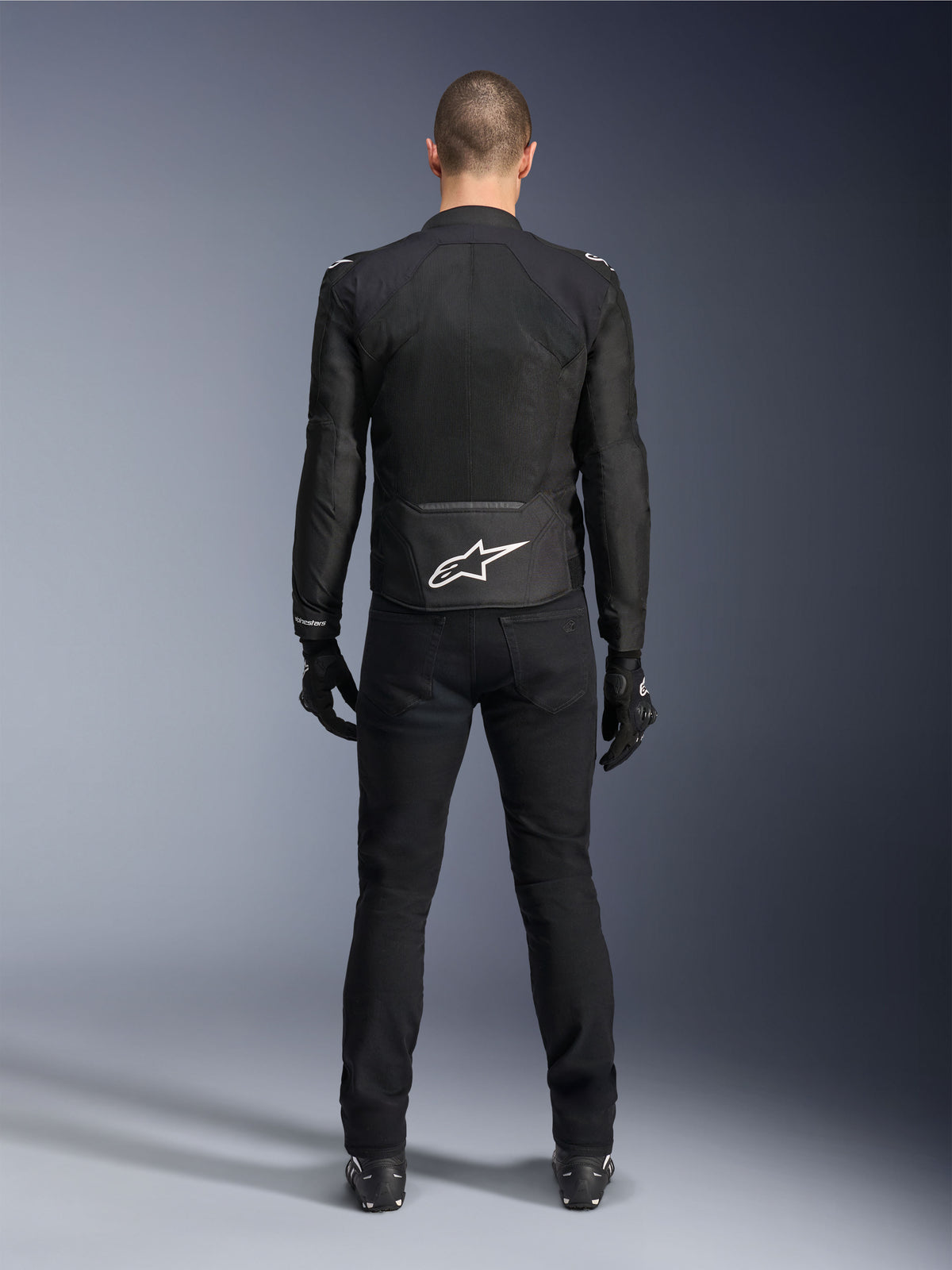 Giacca Alpinestars Viper Air V4, giacca da moto in tessuto nero, vista posteriore con logo a stella Alpinestars bianco sulla parte inferiore della schiena, indossata con pantaloni e guanti neri, abbigliamento estivo per guida stradale e sportiva