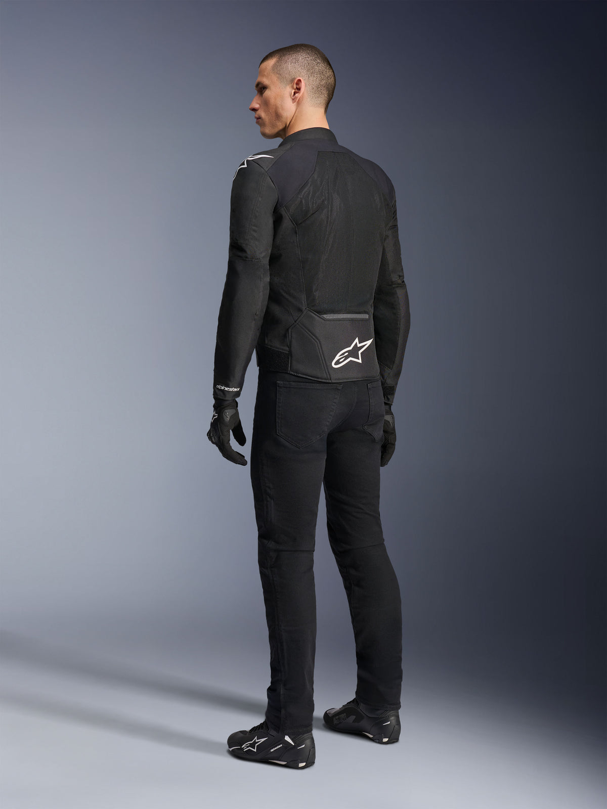 Giacca Alpinestars Viper Air V4, giacca da moto in tessuto nero, vista posteriore su un modello, con ampi pannelli in rete tecnica per la ventilazione e logo a stella bianco sulla parte bassa della schiena, indossata con pantaloni e guanti neri abbinati