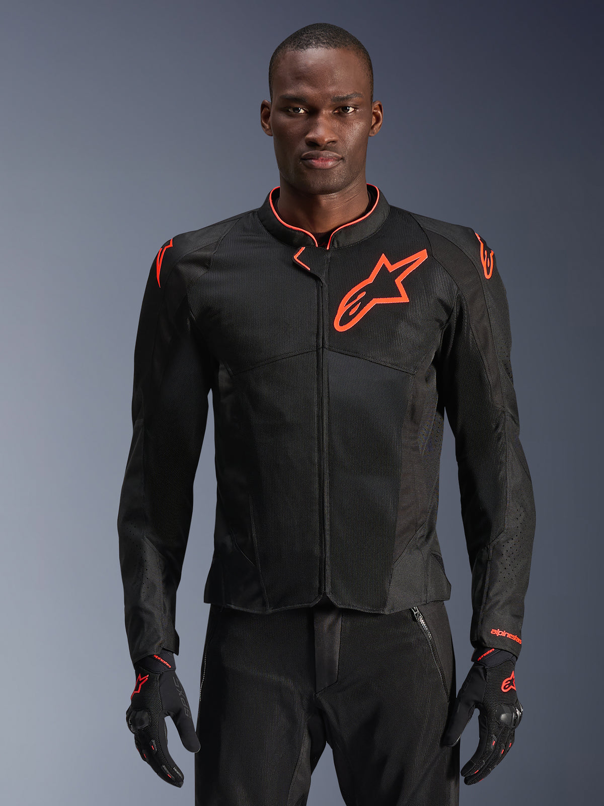 Giacca Alpinestars Viper Air V4, giacca da moto nera e rosso fluo, costruzione in mesh ventilato con logo a stella rosso in evidenza, indossata da un modello con guanti coordinati, design sportivo performante