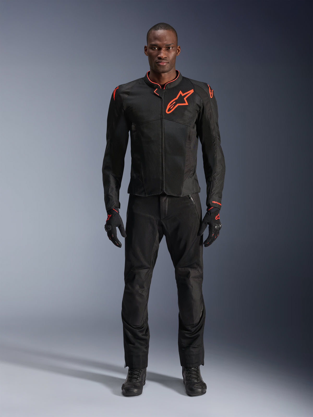Giacca Alpinestars Viper Air V4 in Nero Rosso Fluo, indossata da un modello con pantaloni e guanti neri coordinati, dotata di pannelli in mesh per la circolazione dell'aria e un evidente logo Alpinestars rosso sul petto, abbigliamento sportivo da moto da strada.