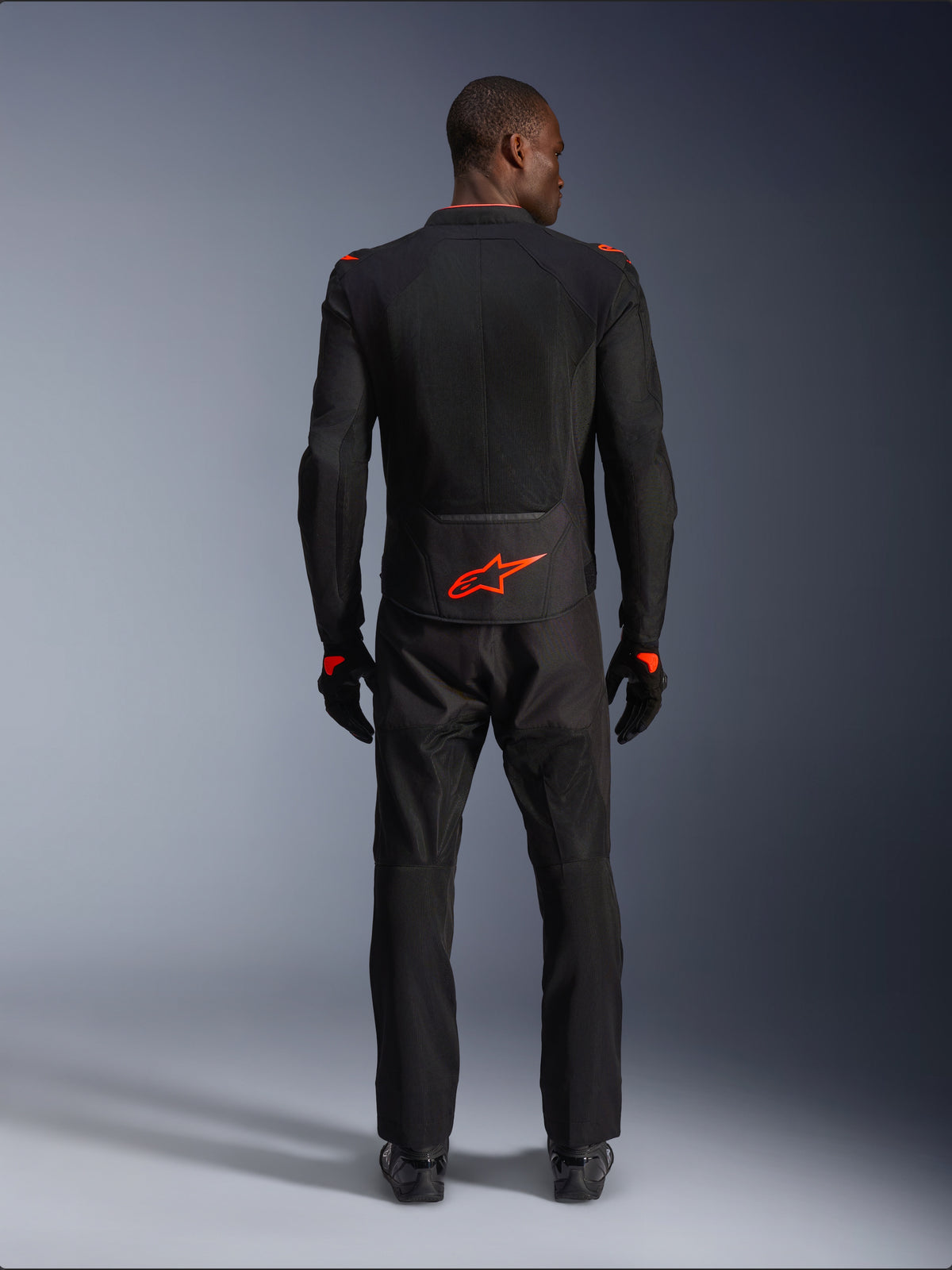 Alpinestars Viper Air V4 Jacket, nero e rosso fluo, vista posteriore su modello, indossata con pantaloni da moto e guanti neri coordinati, caratterizzata da un vivace logo rosso fluorescente sulla parte bassa della schiena, costruzione in rete per il flusso d'aria, vestibilità atletica per la guida su strada in moto.