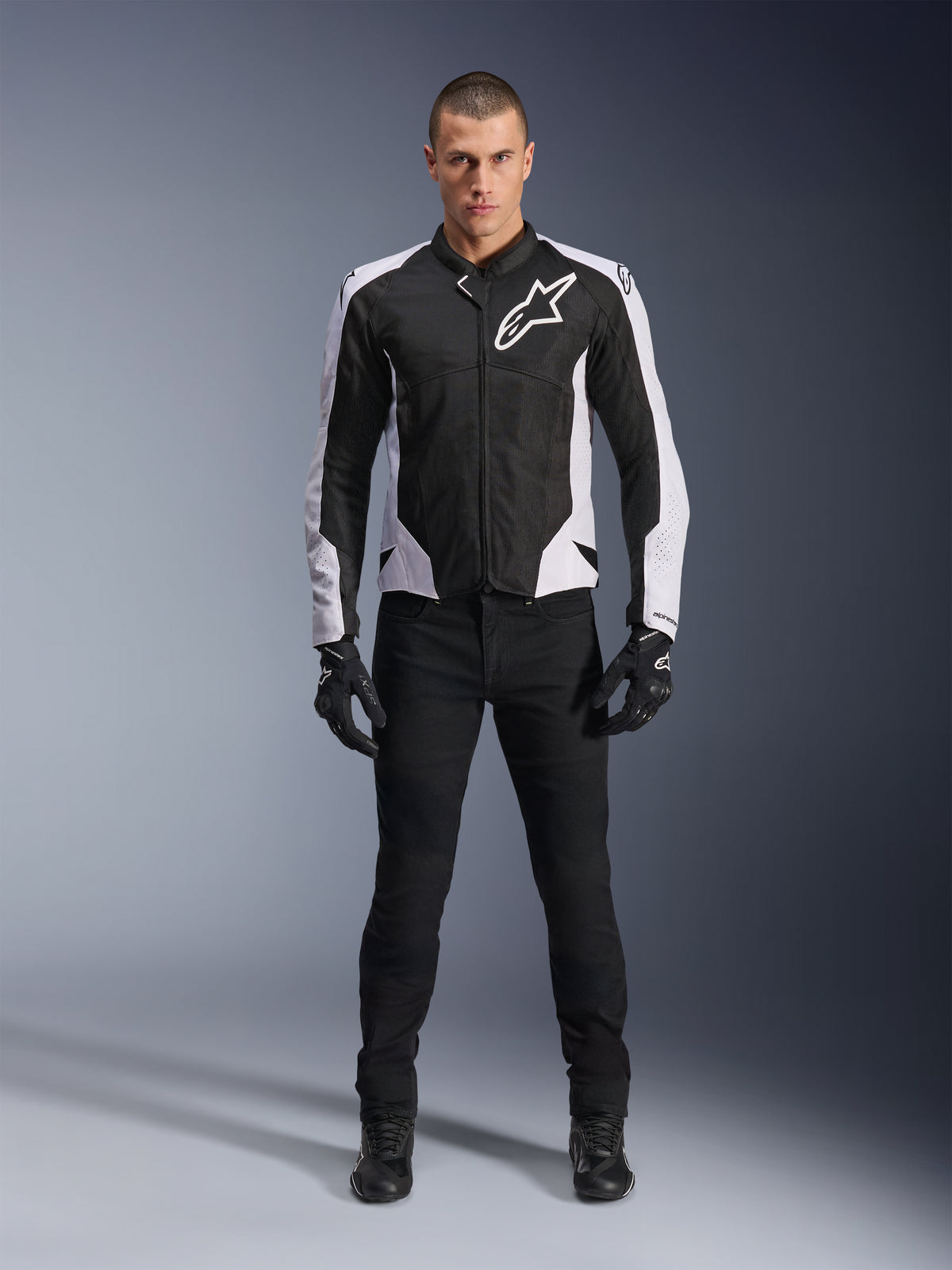 Giacca Alpinestars Viper Air V4, giacca da moto nera e bianca con grande logo bianco sul petto, indossata da un modello con pantaloni e guanti neri, con pannelli in mesh per la ventilazione, abbigliamento sportivo per guida su strada