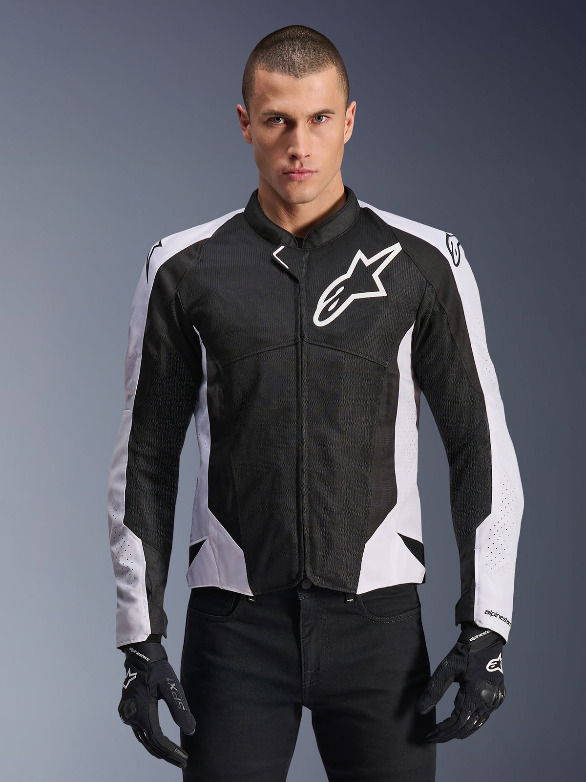 Alpinestars Viper Air V4 Jacket, giacca da moto racing, nero e bianco, indossata da un pilota, costruzione in mesh tecnico e tessuto con pannelli bianchi sulle spalle, logo a stella prominente sul petto, design sportivo, abbinata a guanti da moto neri