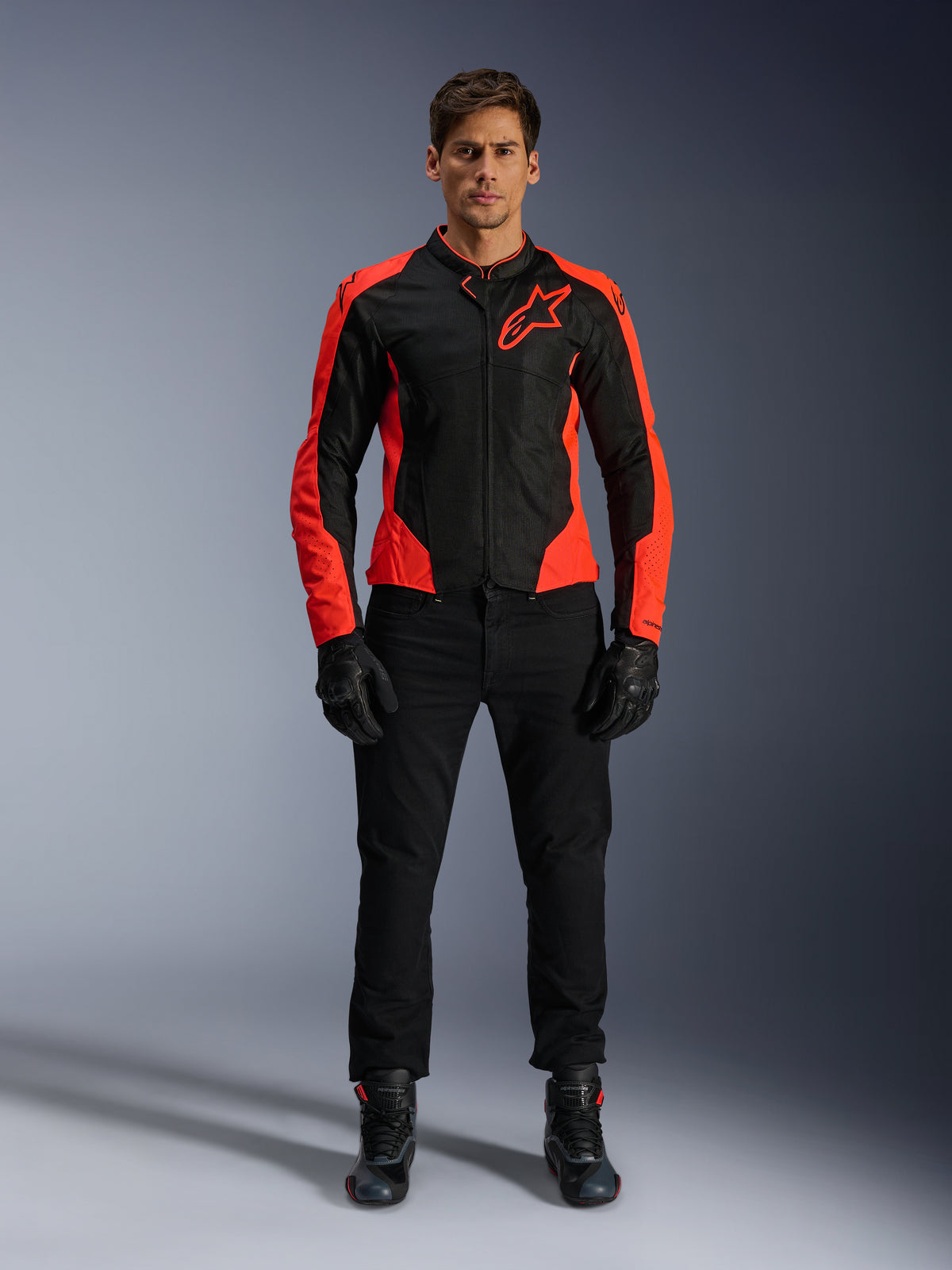 Modello che indossa la giacca Alpinestars Viper Air V4 in rosso fluo e nero, abbinata a pantaloni da moto, guanti e stivali neri, con pannelli in mesh traspirante per la ventilazione e un audace logo a stella sul petto, abbigliamento sportivo da moto da strada