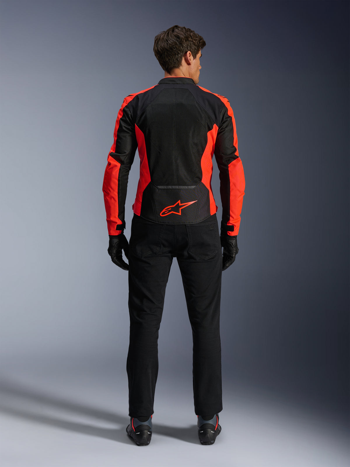 Giacca Alpinestars Viper Air V4, rosso fluo e nero, vista posteriore con ampi pannelli in mesh tecnico e accenti laterali in rosso fluorescente, logo Alpinestars rosso sulla parte bassa della schiena, indossata con pantaloni da guida e guanti neri.