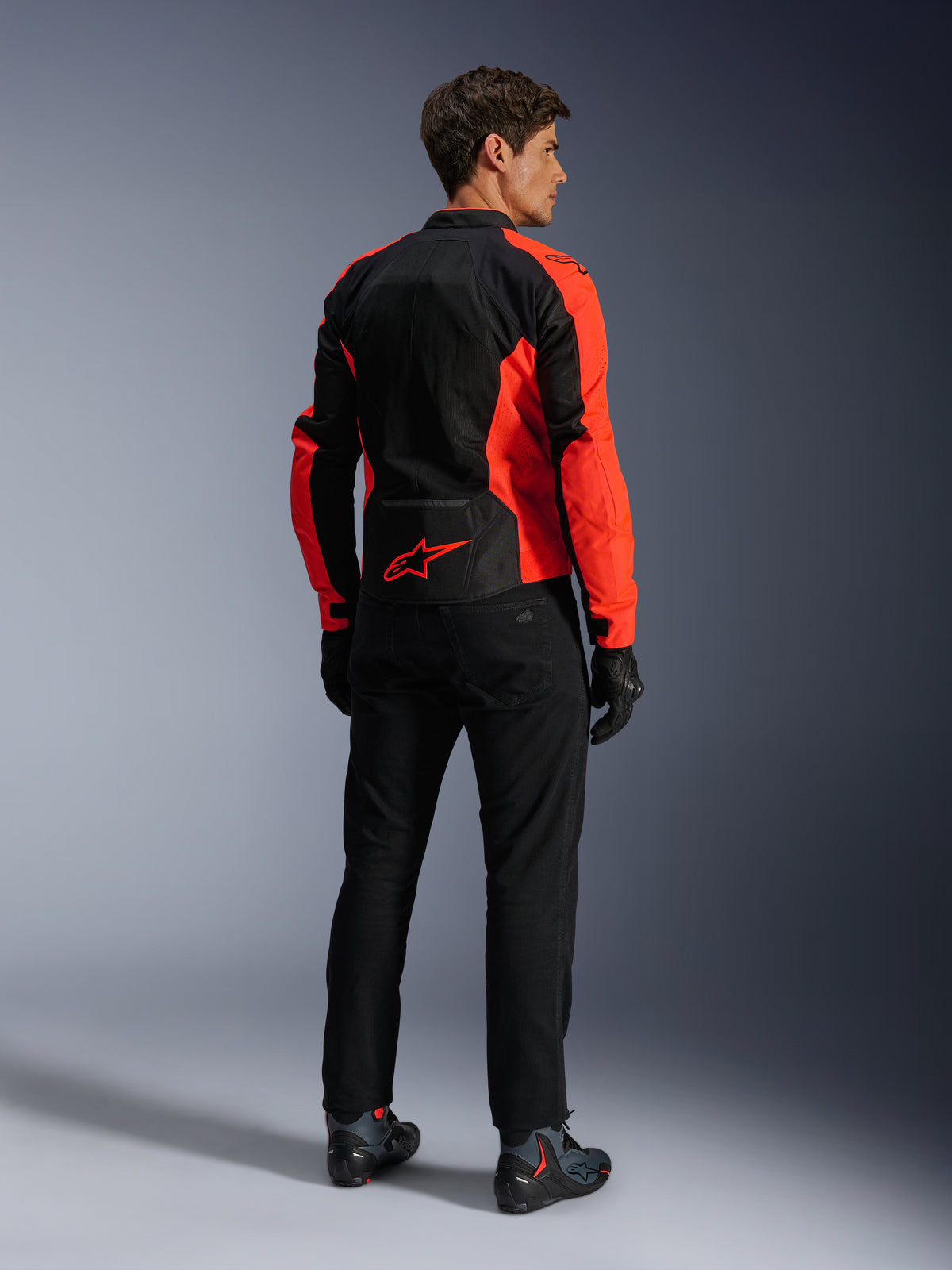Giacca Alpinestars Viper Air V4, Rosso Fluo Nero, vista posteriore su modello, con pannelli in rete tecnica e logo a stella rosso sulla parte inferiore della schiena, abbinata a pantaloni e guanti da moto neri per un look completo da strada.