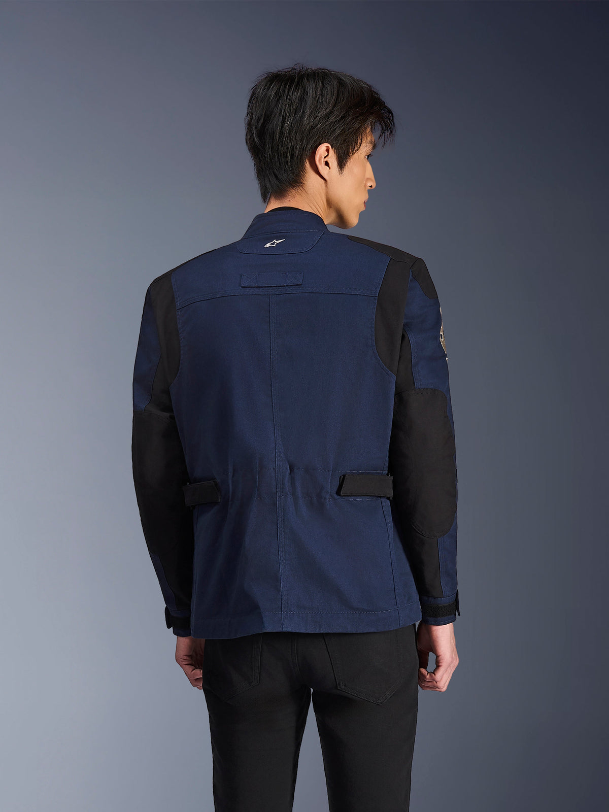 Alpinestars Dice Jacket, giacca da moto urbana stile field blu scuro e nera, vista posteriore indossata da un uomo, con pannelli neri rinforzati su spalle e gomiti e linguette di regolazione in vita.