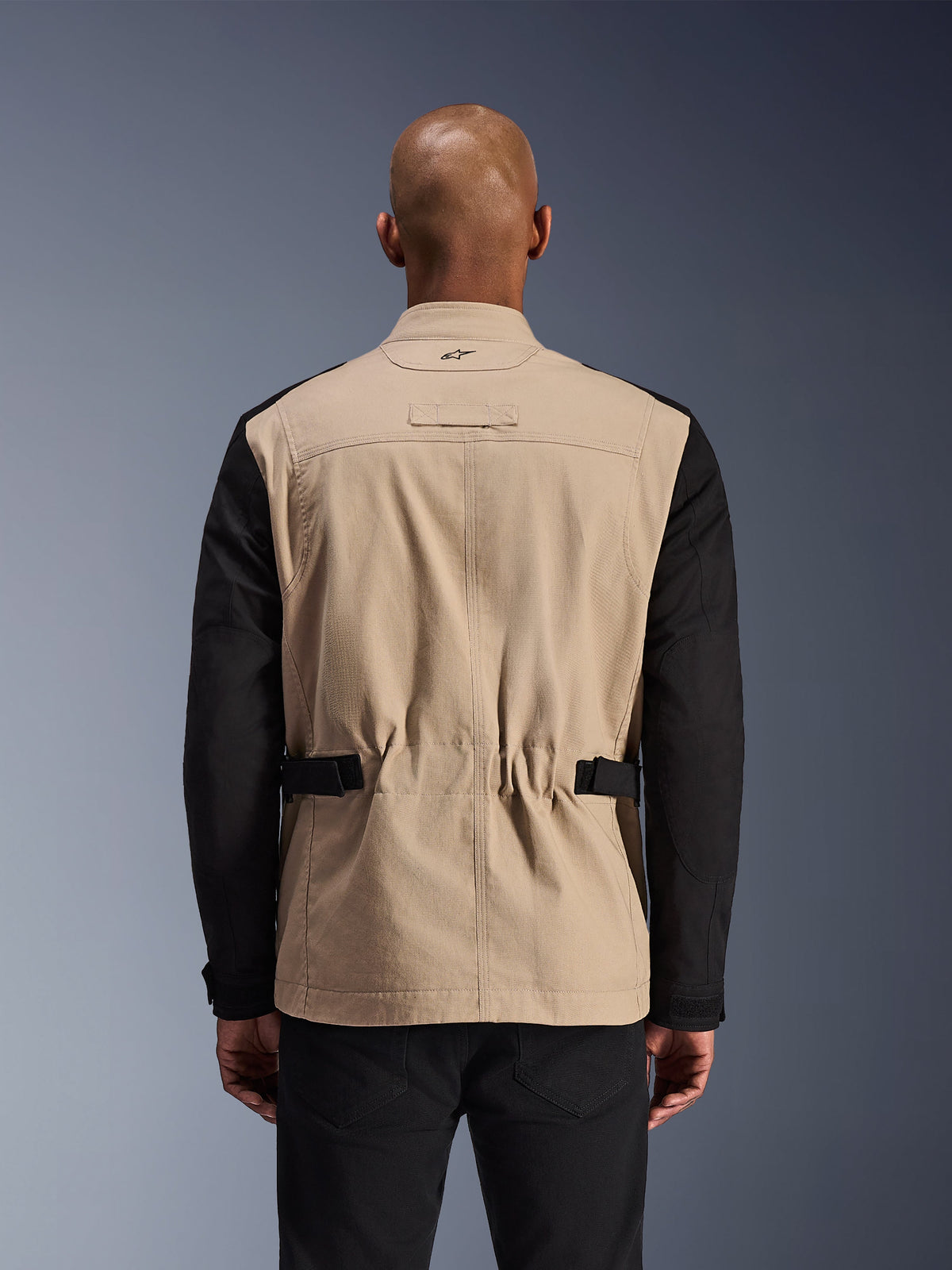 Alpinestars Dice Jacket, giacca da moto urbana, alluminio e nero, vista posteriore su un modello, con spalle plissettate per la mobilità, cinturini regolabili in vita e una robusta costruzione in twill di policotone.