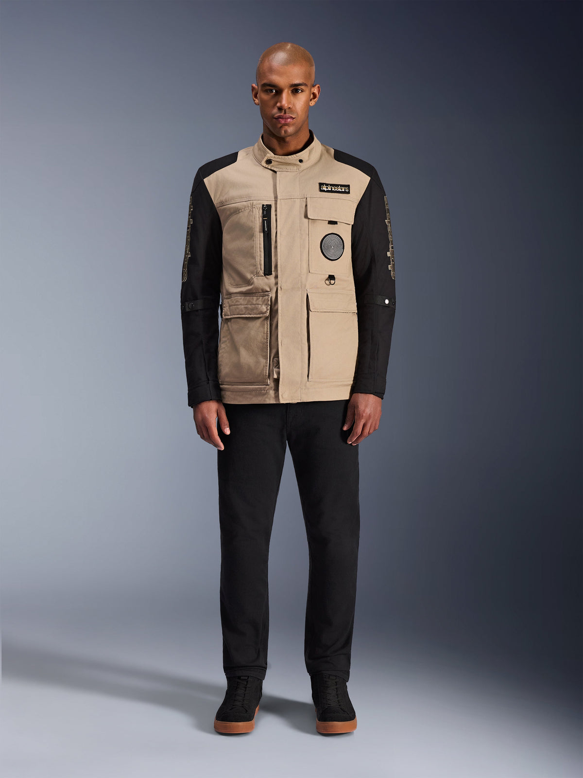 Giacca Alpinestars Dice, giacca da moto urbana, corpo color alluminio con maniche nere, silhouette ispirata al workwear con quattro tasche utility frontali, indossata con pantaloni neri e sneaker alte nere, abbigliamento tecnico da moto robusto in stile urban