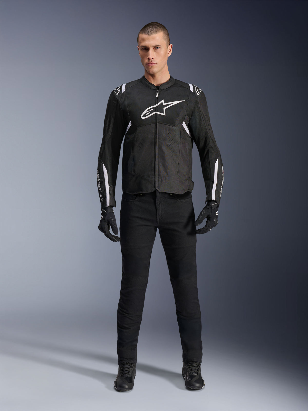 Giacca Alpinestars T-Sps Air V2, giacca da moto in tessuto nero e bianco, caratterizzata da un grande logo bianco sul petto e pannelli in mesh, indossata da un modello con equipaggiamento nero per la guida sportiva urbana