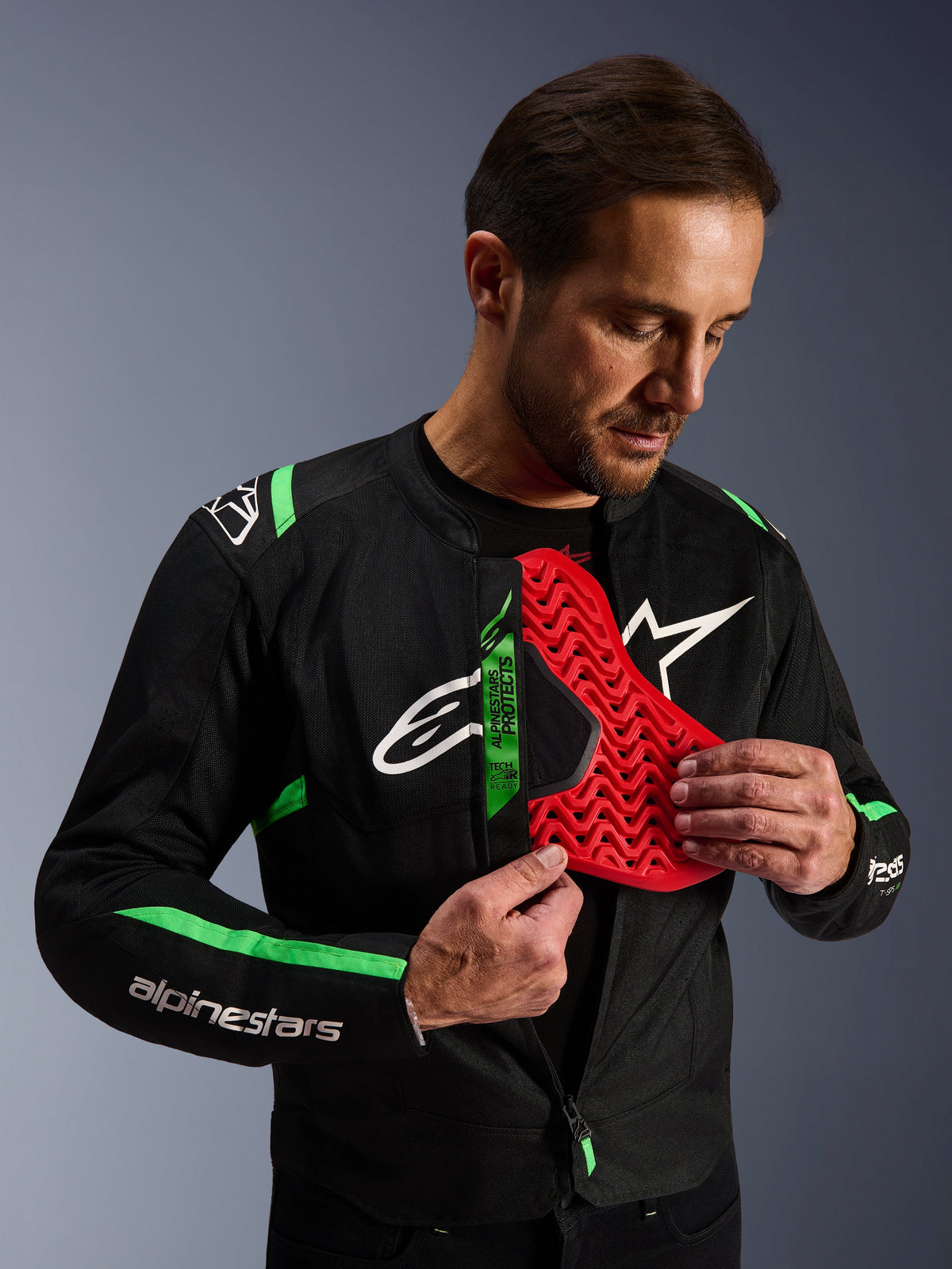 Giacca Alpinestars T-SPS Air V2, giacca da moto nero e verde fluo, uomo che mostra l'inserto della protezione toracica Nucleon rosso, etichetta Tech-Air Ready, design sportivo in tessuto con pannelli in rete