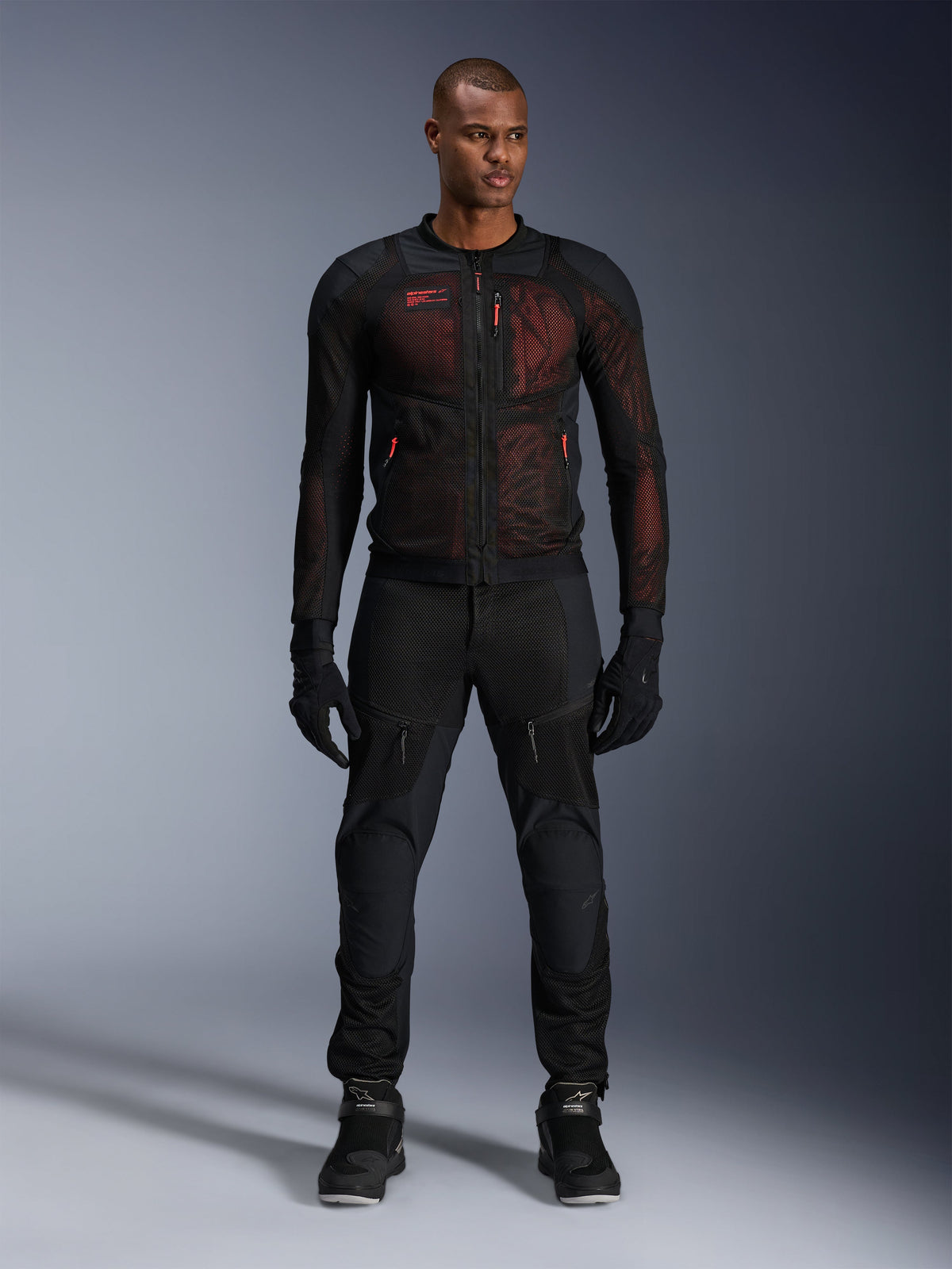 Giacca Alpinestars Troop-Air Pro, giacca tecnica traforata e corazzata, nero e rosso fluo, indossata da un modello con pantaloni e guanti coordinati, con pannelli in mesh ad alta ventilazione e accenti rossi, abbigliamento moto urban