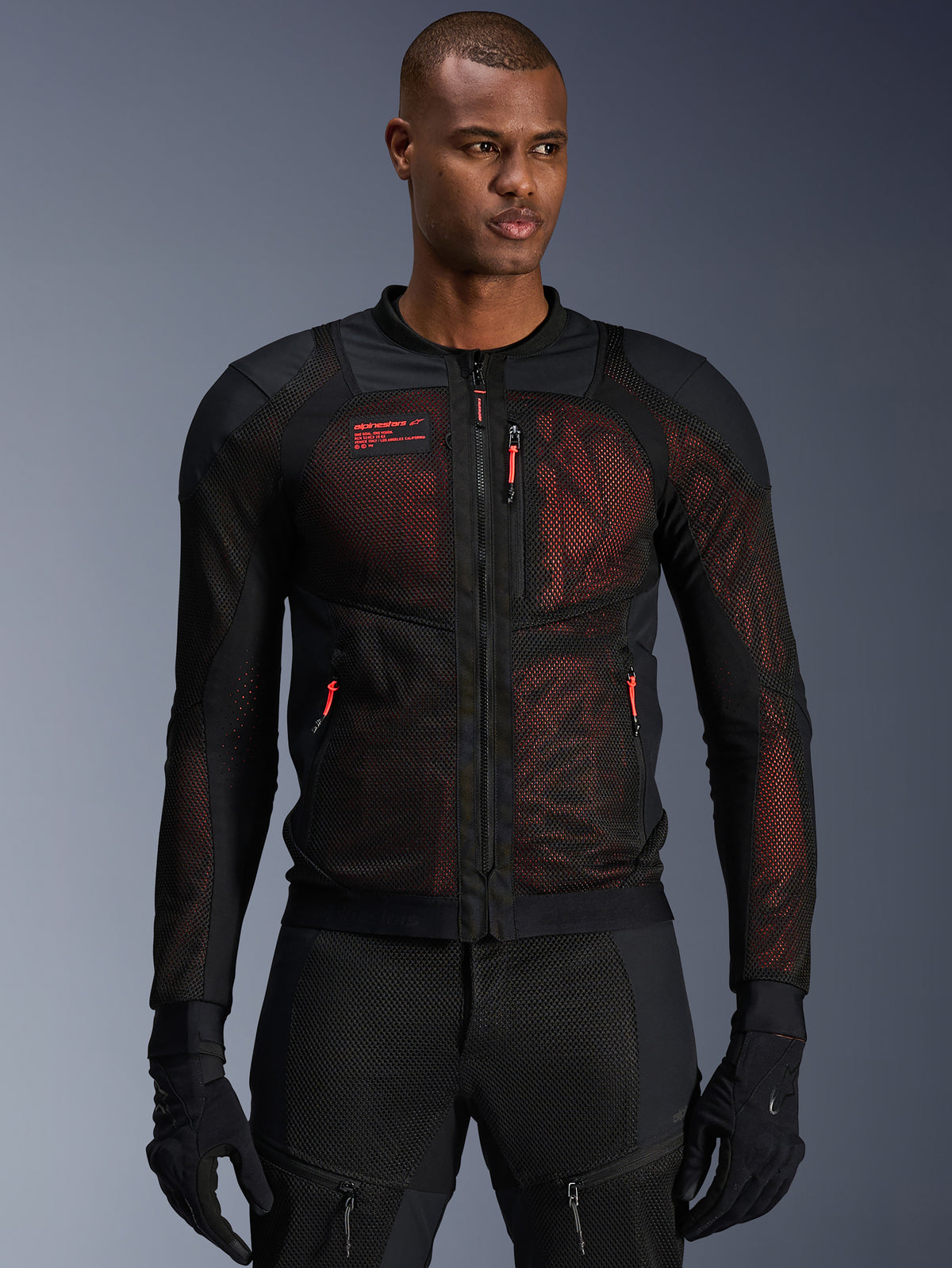 Alpinestars Troop-Air Pro Jacket, giacca da moto tecnica corazzata, nero e rosso fluo, dotata di tiretti delle cerniere rossi e logo Alpinestars, pannelli in mesh traspirante con sottostrato rosso, indossata con pantaloni e guanti da moto neri coordinati