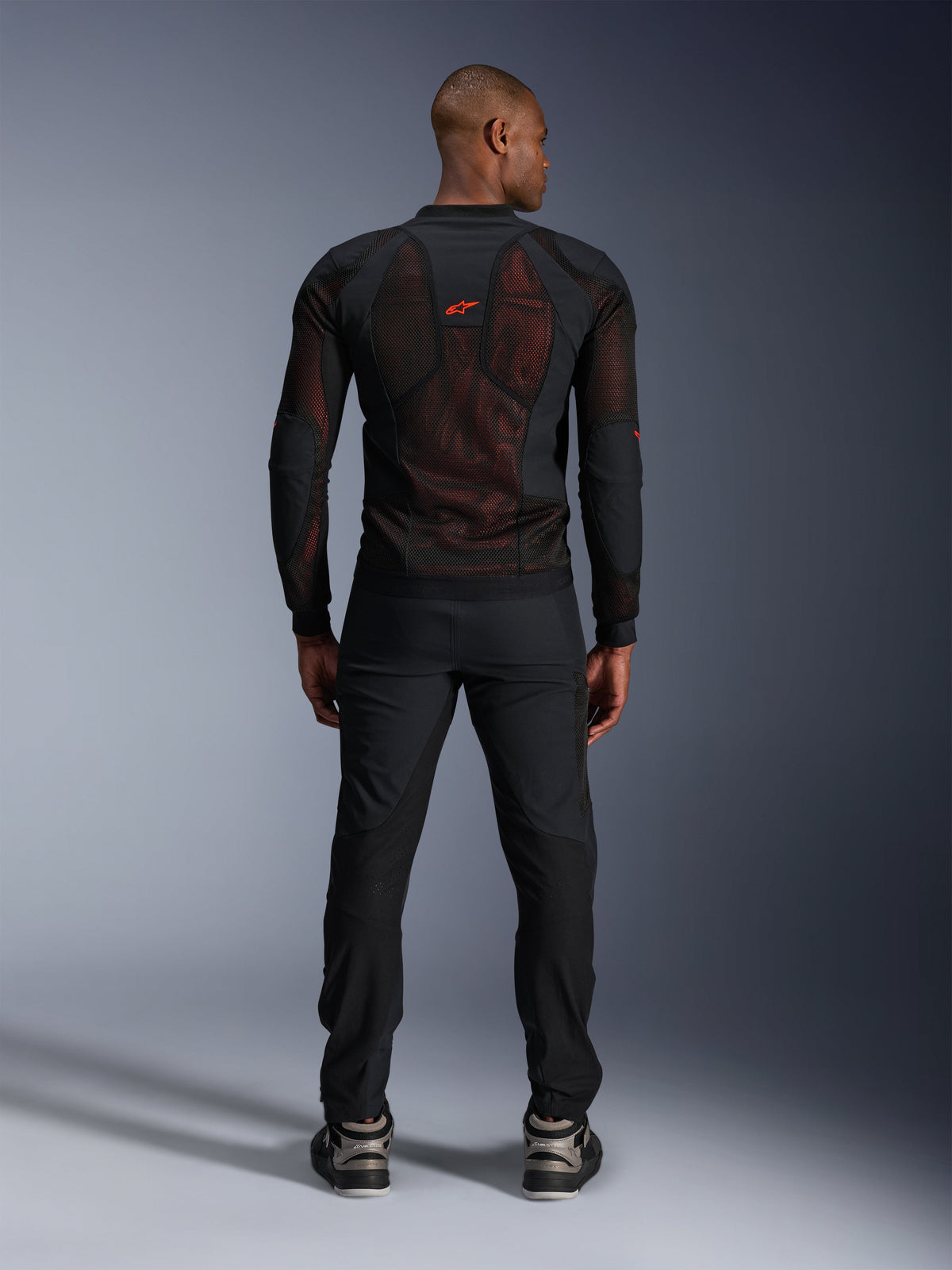 Alpinestars Giacca Troop-Air Pro in Black Red Fluo, vista posteriore su modello, giacca tecnica in mesh con protezioni e pannelli traspiranti, logo rosso sulla parte superiore della schiena, indossata con pantaloni neri e sneaker, abbigliamento motociclistico urbano