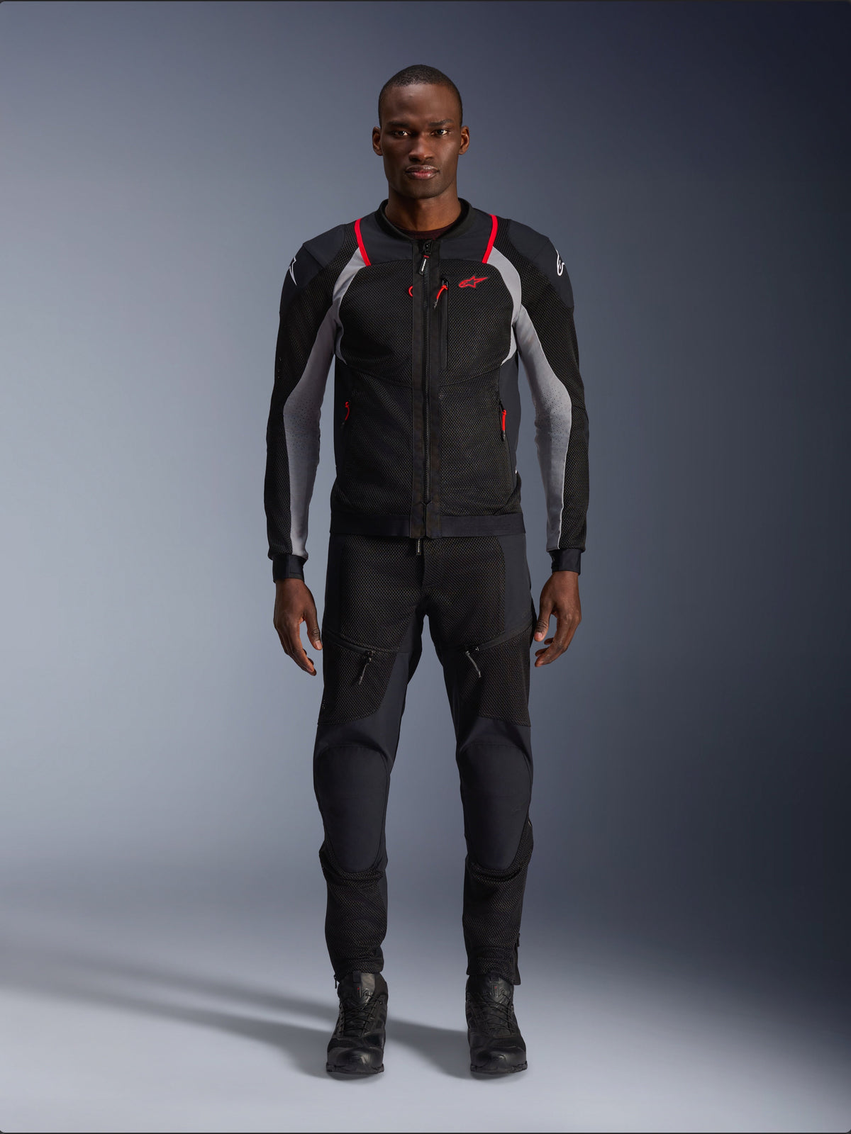 Alpinestars Troop-Air Pro Jacket, giacca tecnica da moto, nero, grigio cenere e rosso brillante, con pannelli in mesh e dettagli rossi, indossata da un modello con pantaloni e stivali da moto neri, design urbano elegante con ventilazione tecnica.