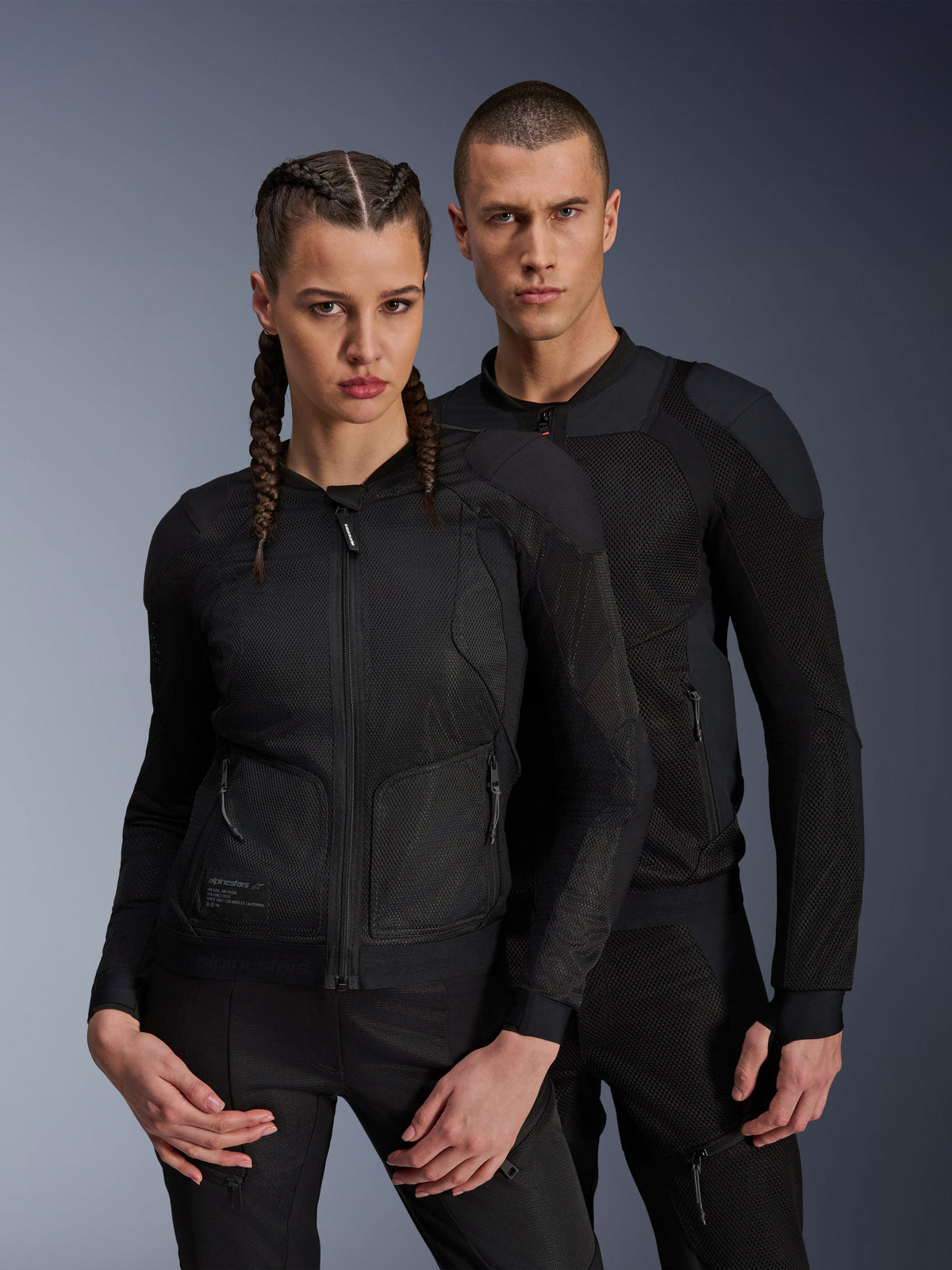Giacca Alpinestars Troop-Air Pro, giacche tecniche corazzate nere indossate da modelli uomo e donna, con pannelli in mesh traspirante e protezioni integrate, abbigliamento da moto urban progettato per la guida in climi caldi.