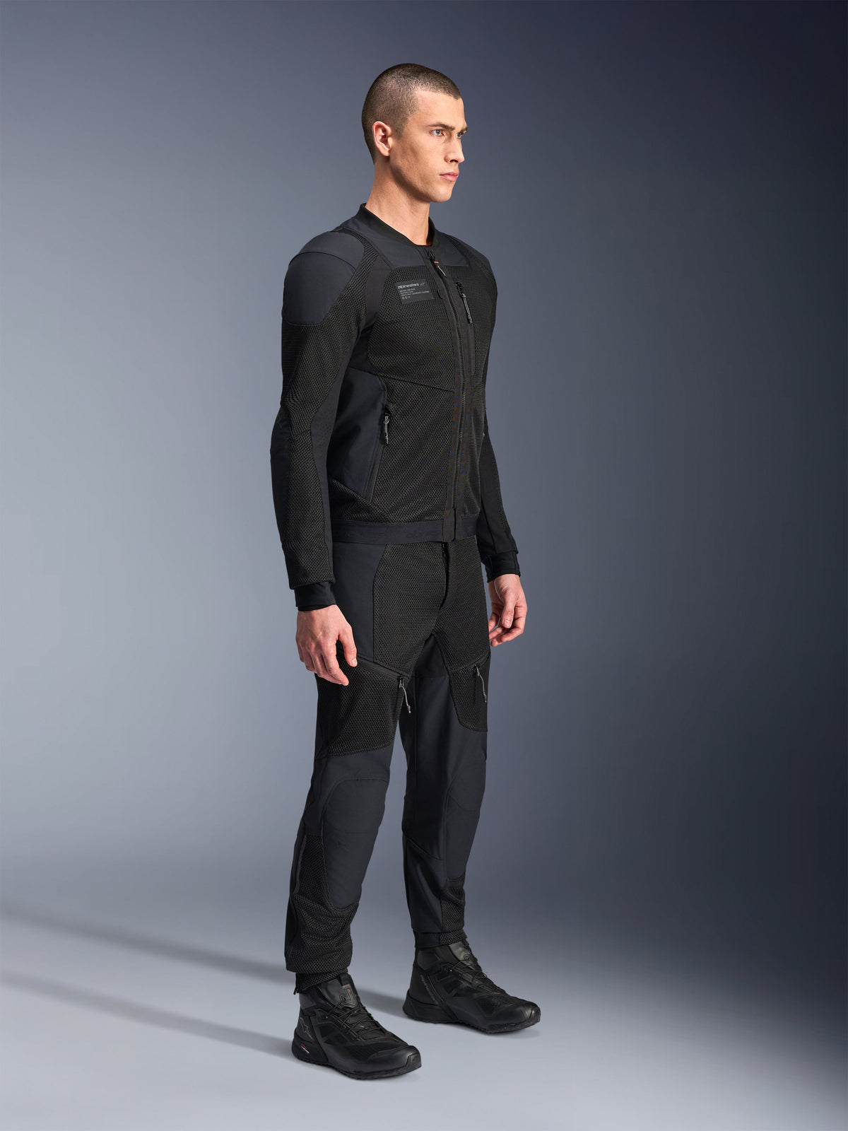 Giacca Alpinestars Troop-Air Pro, giacca d'aria corazzata tecnica, nera, indossata da un modello con pantaloni da moto e stivali neri abbinati, caratterizzata da una struttura avanzata in mesh tecnologico 2D e pannelli di ventilazione traspiranti, abbigliamento da moto urban contemporaneo.