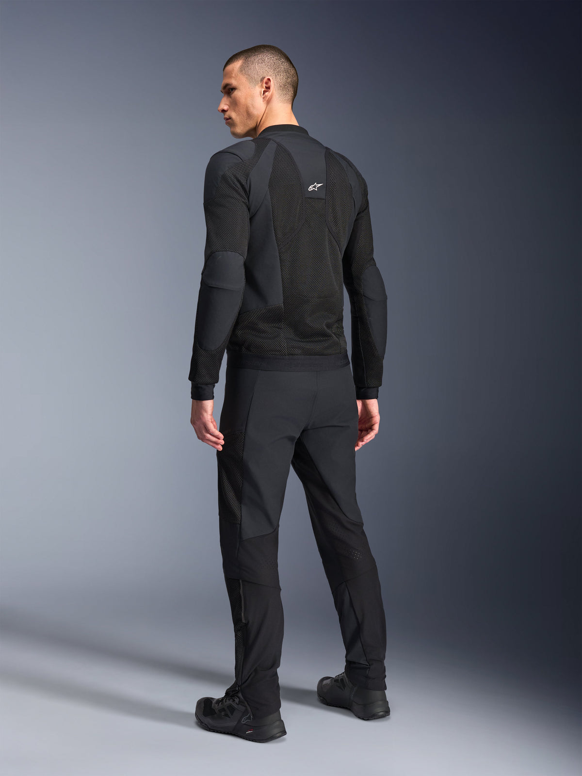 Alpinestars Troop-Air Pro Jacket, nera, giacca tecnica ventilata vista dal retro, con ampi pannelli in mesh per la circolazione dell'aria, abbinata a pantaloni tecnici e scarpe neri coordinati.