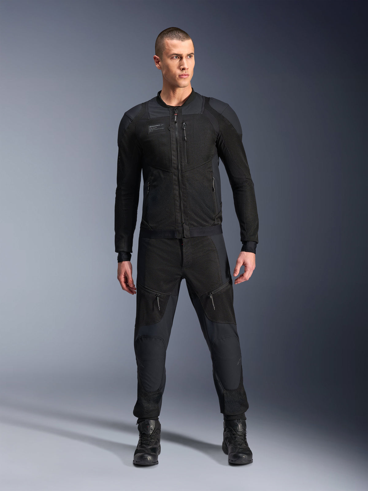 Giacca Alpinestars Troop-Air Pro, giacca tecnica da moto corazzata nera, caratterizzata da pannelli in mesh e cerniere frontali, indossata con pantaloni neri coordinati e stivali da guida, abbigliamento stradale urbano premium