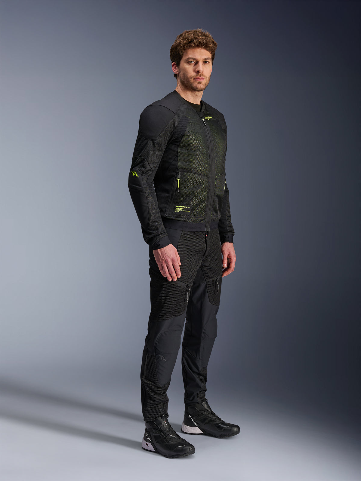 Giacca Alpinestars Troop-Air, giacca moto in mesh, nero e giallo fluo, indossata da un modello con pantaloni neri e scarpe da moto coordinati, caratterizzata da una struttura in mesh ad alto flusso d'aria con accenti giallo fluorescente su petto e maniche, design tecnico leggero per la guida su strada