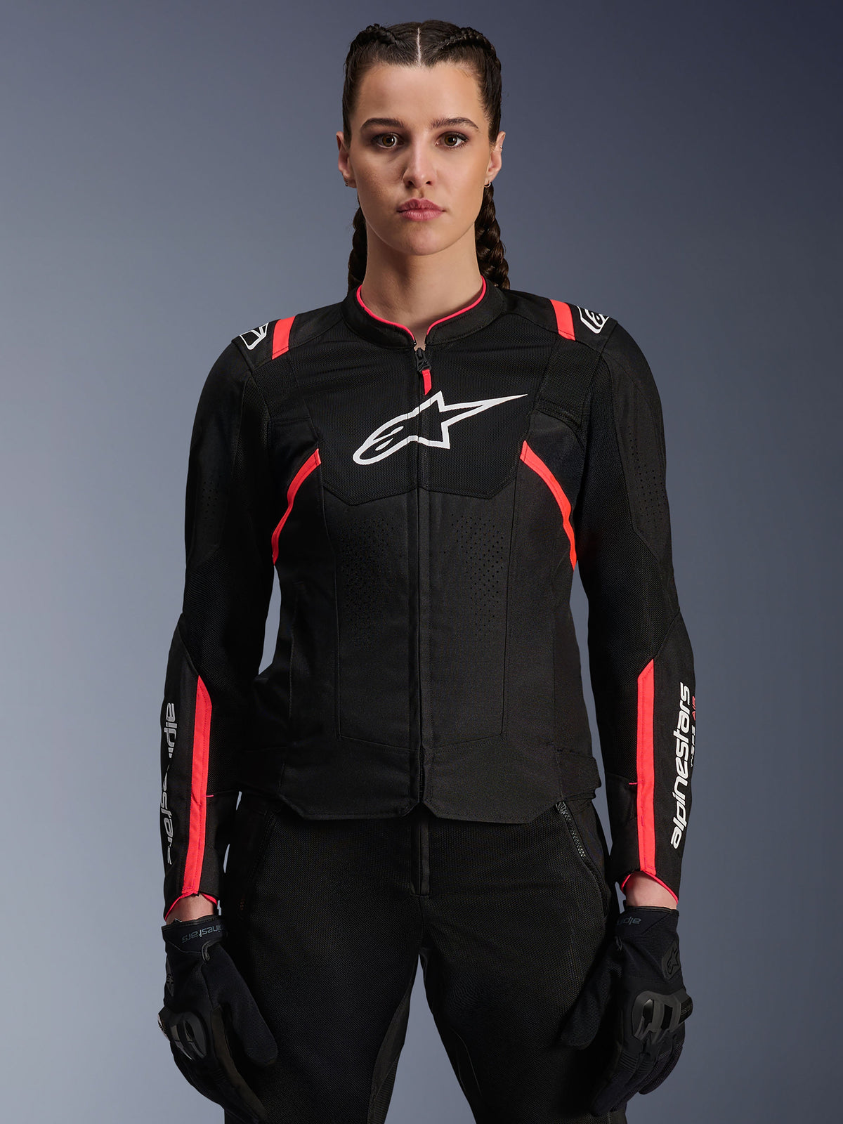 Giacca Alpinestars Stella T-Sps Air V2 da donna, nero e Diva Pink, giacca da moto in tessuto con pannelli in mesh traspirante e accenti rosa, logo Alpinestars bianco sul petto, indossata da una modella con pantaloni e guanti da guida neri.