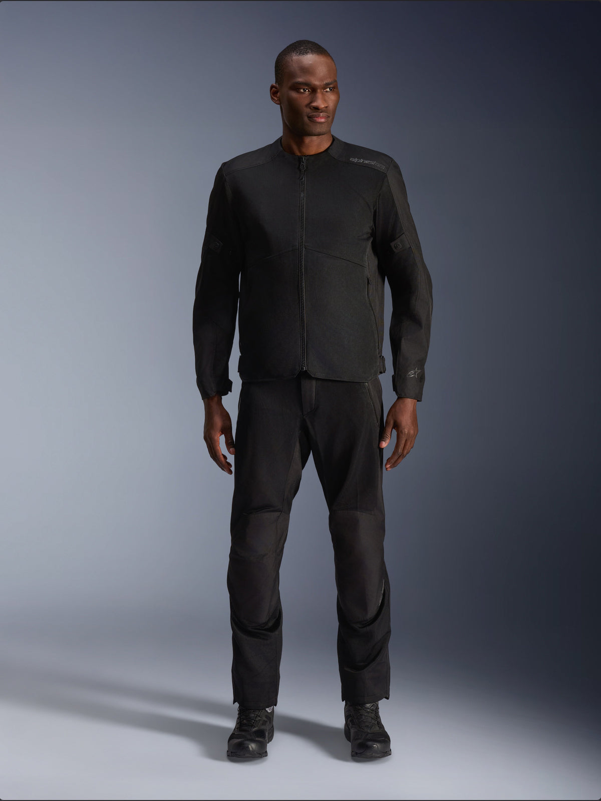Modello che indossa la giacca Alpinestars C-1 Air in nero, abbinata a pantaloni e stivali neri coordinati, abbigliamento da moto urbano per il commuting, estetica pulita con pannelli in rete e loghi discreti