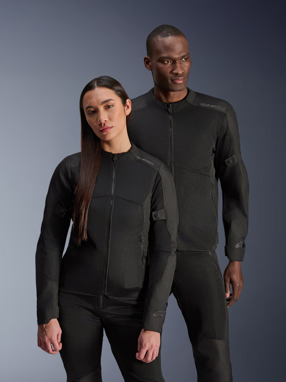 Un uomo e una donna con indosso le giacche Alpinestars C-1 Air e Stella C-1 Air, giacche da moto urban coordinate in tessuto nero con pannelli in rete per la ventilazione, abbinate a pantaloni da guida neri per un look pulito e contemporaneo.