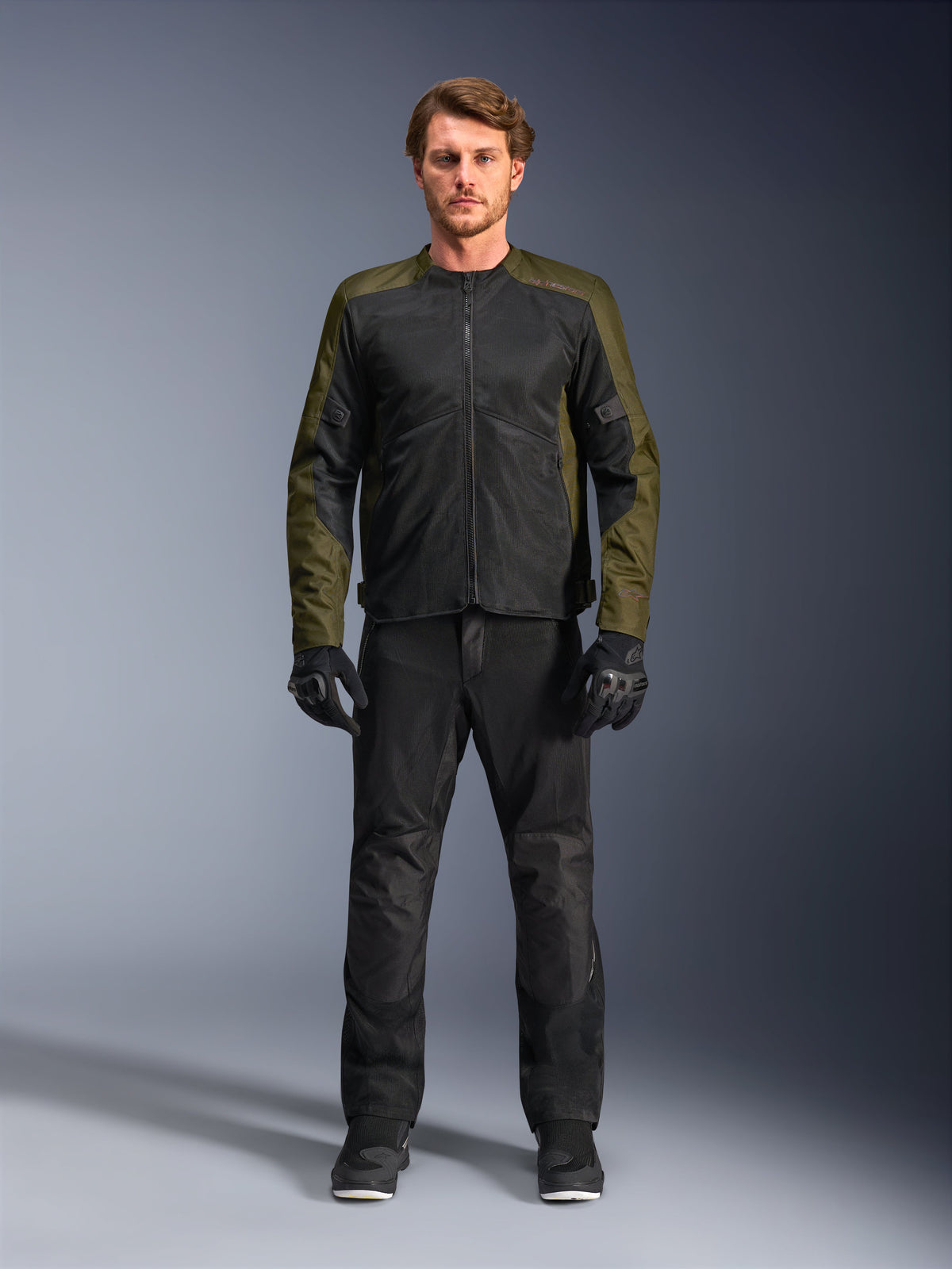Giacca Alpinestars C-1 Air, kaki e nero, indossata da un modello con pantaloni da moto e guanti neri, design in tessuto leggero con pannelli in mesh tecnica, abbigliamento urbano contemporaneo per motociclisti